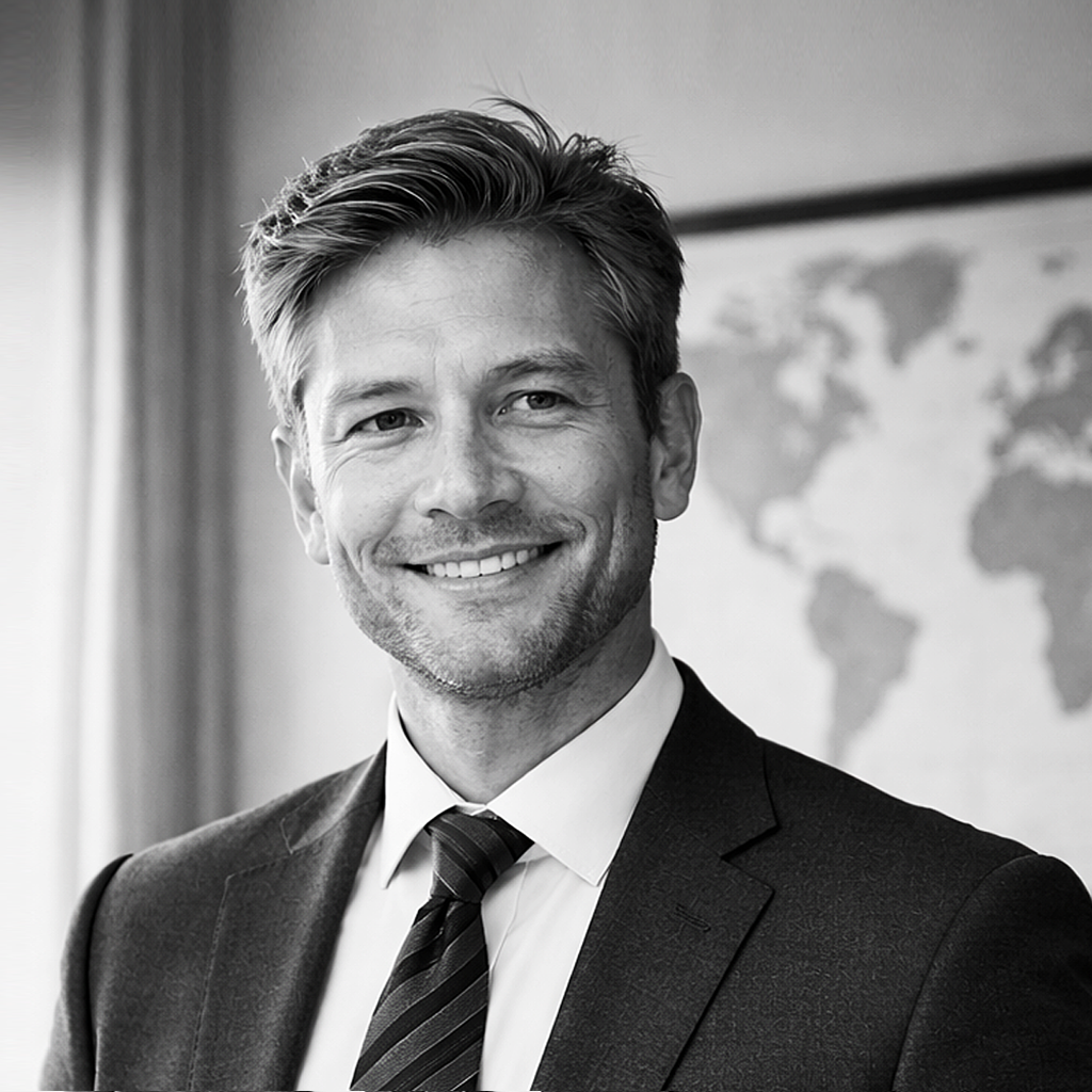 Black and white portrait of a smiling man in a business suit, standing indoors with a world map in the background.
