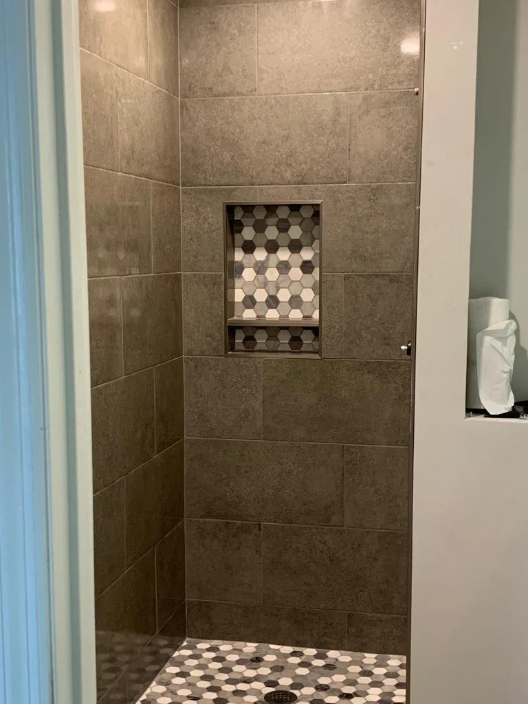 A tiled shower with brown wall tiles, a built-in niche with hexagonal tiles, and a floor with small hexagonal tiles in black, white, and gray.