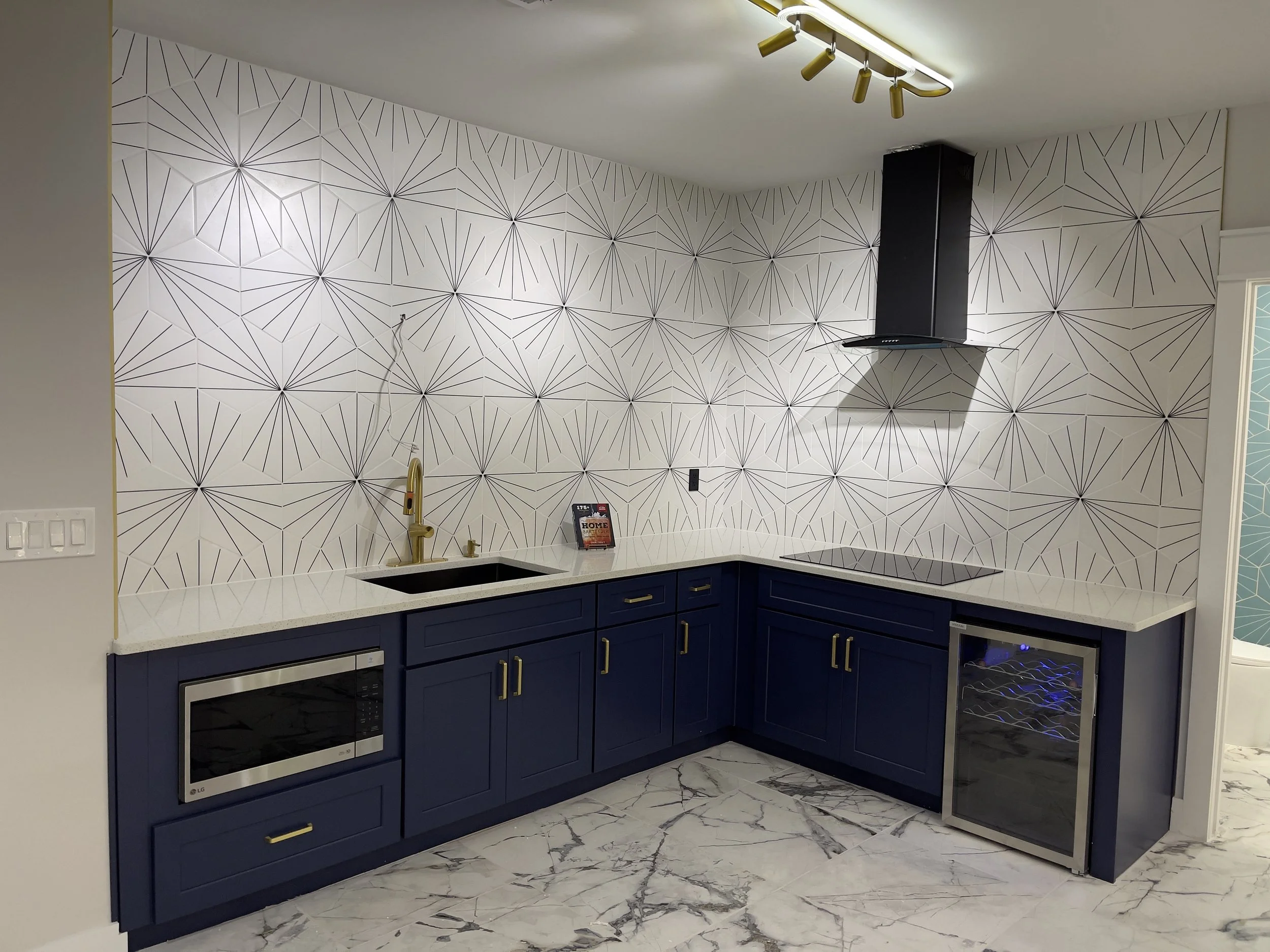 Modern kitchen with navy blue cabinets, white marble countertops, and a geometric patterned white and black wall.