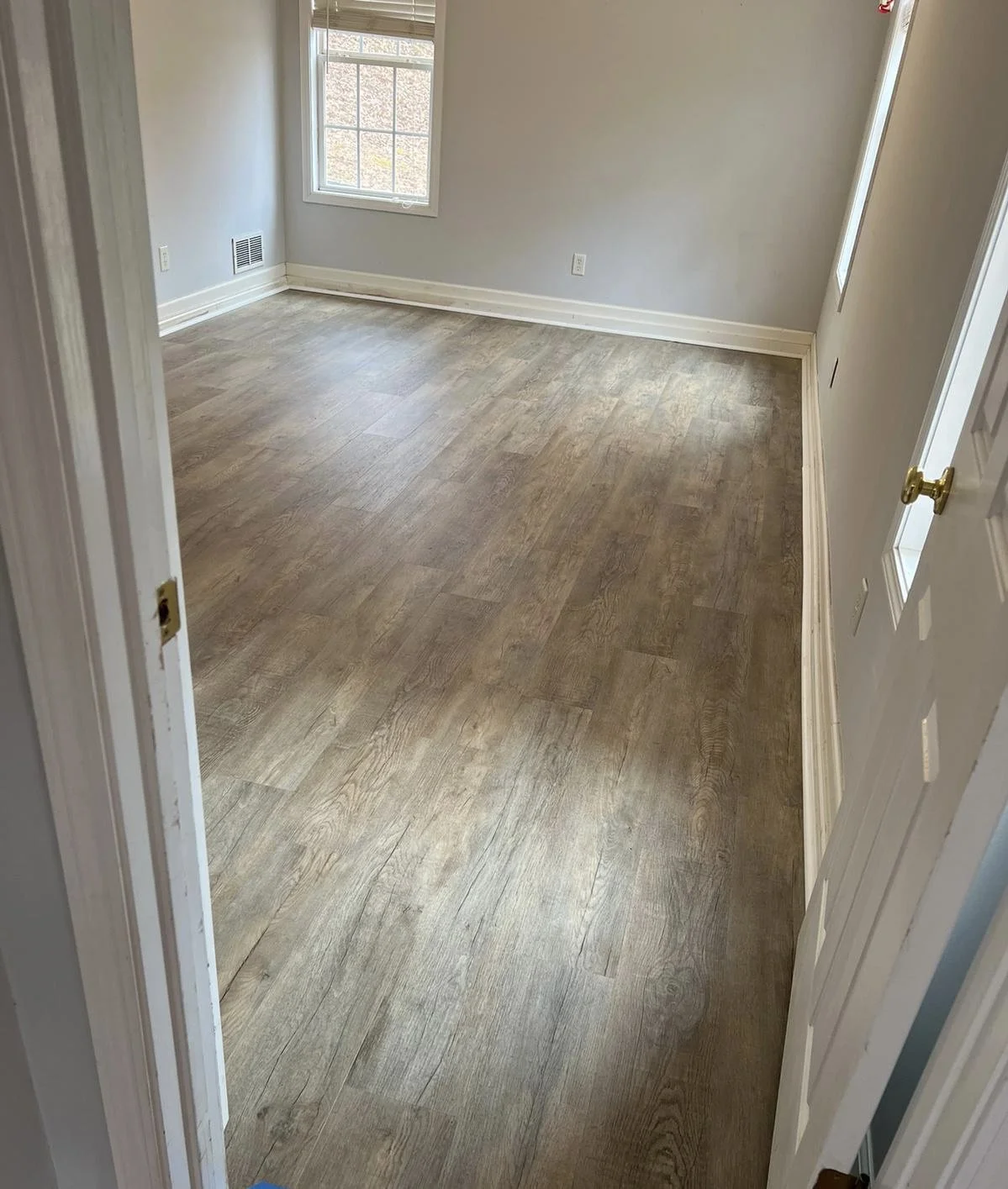 Empty room with wood laminate flooring, white walls, a window, and white baseboards.
