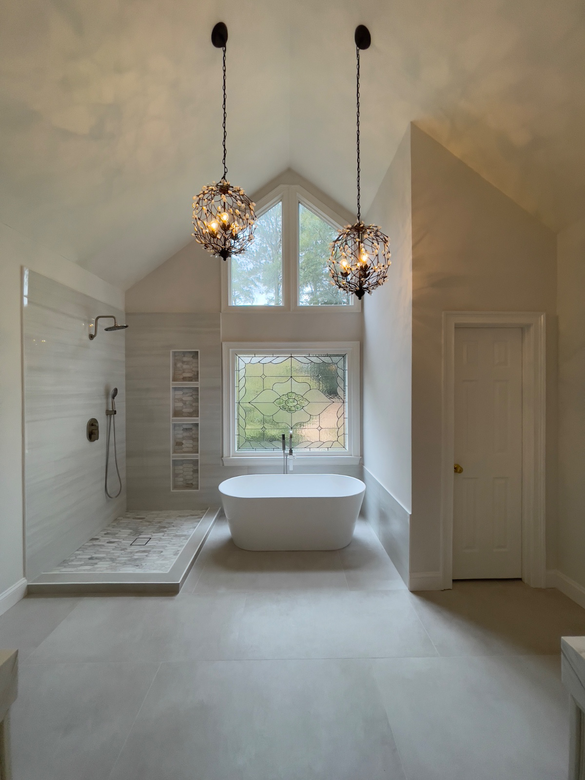 Modern bathroom with a freestanding bathtub, walk-in shower, large windows, and two decorative pendant lights hanging from the ceiling.