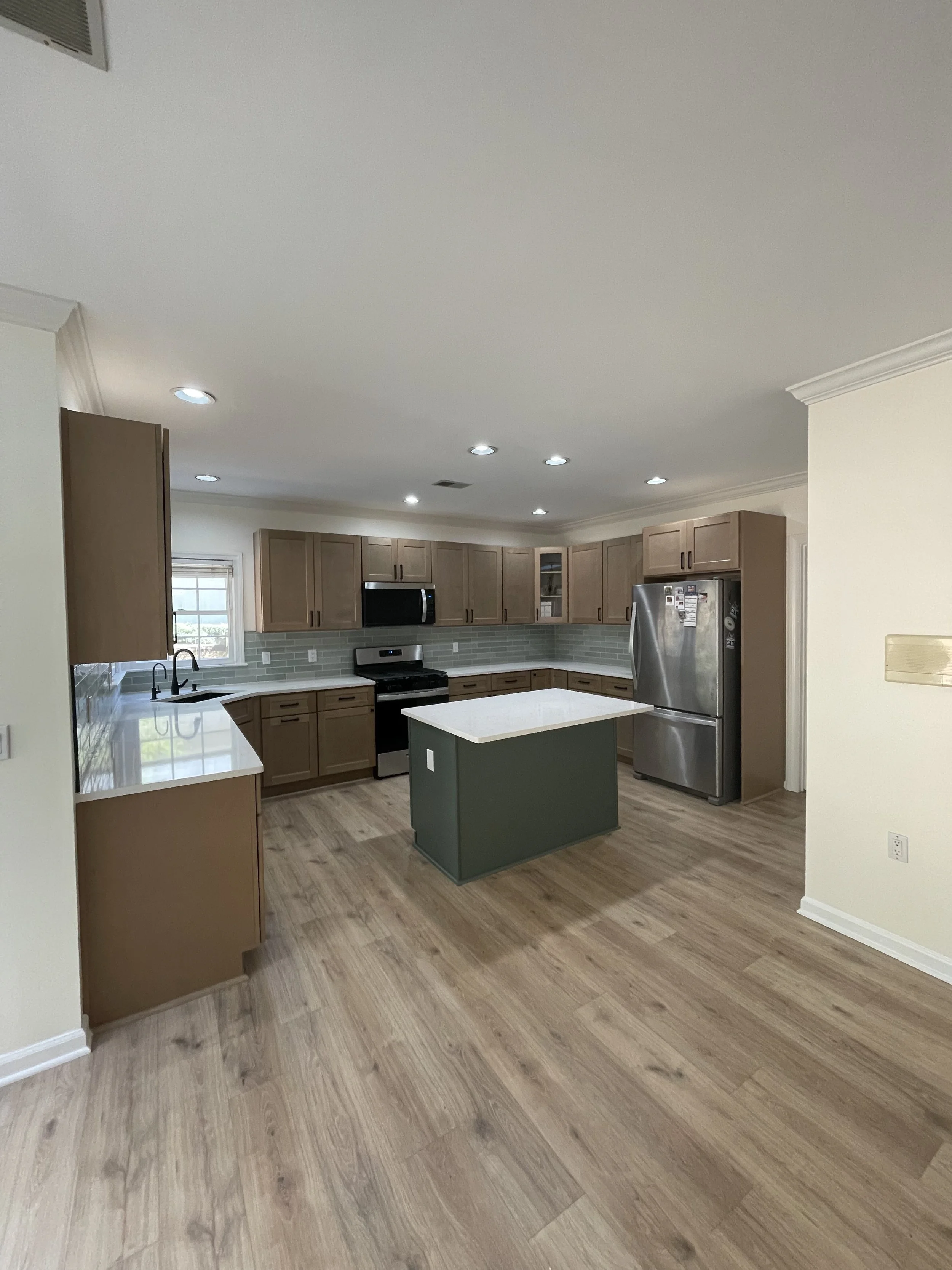 Modern kitchen with wooden cabinets, stainless steel appliances, a small centered island, and wood flooring.