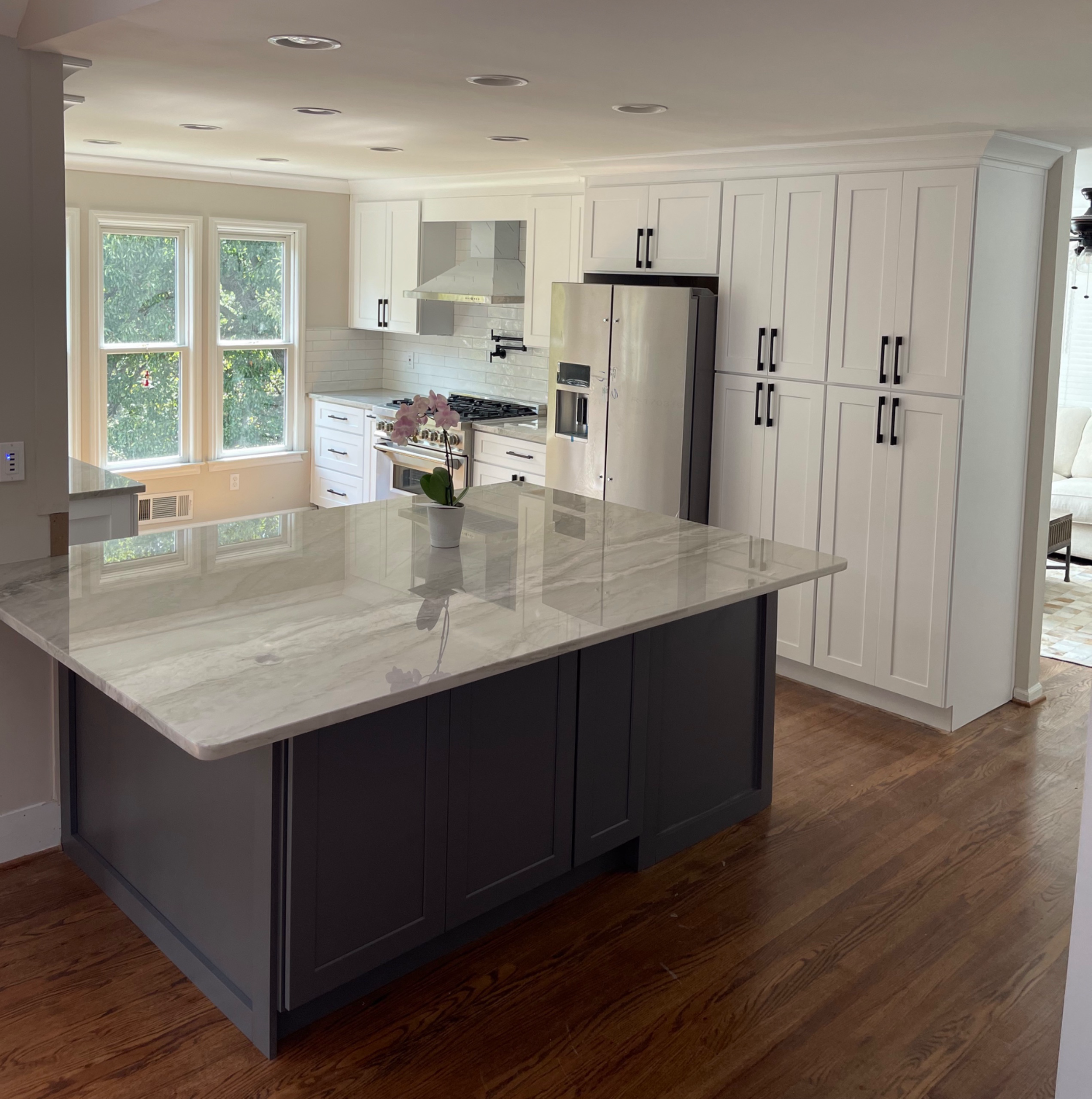 Modern kitchen with white cabinets, stainless steel appliances, a gray island with a marble countertop, and a potted pink orchid on the island.