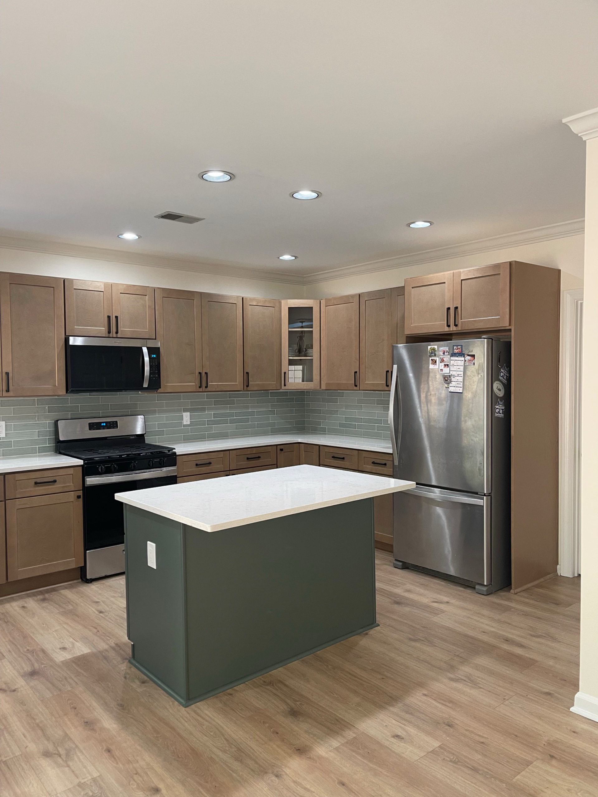 Modern kitchen with wooden cabinets, stainless steel appliances, a kitchen island with a white countertop, wood flooring, and recessed lighting.