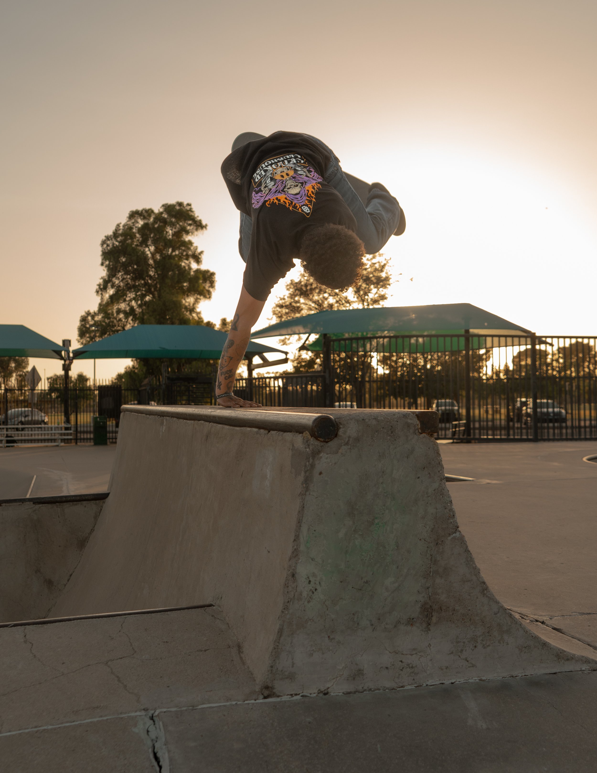 Skateboarder performing a handstand on a ledge at sunset in a park.