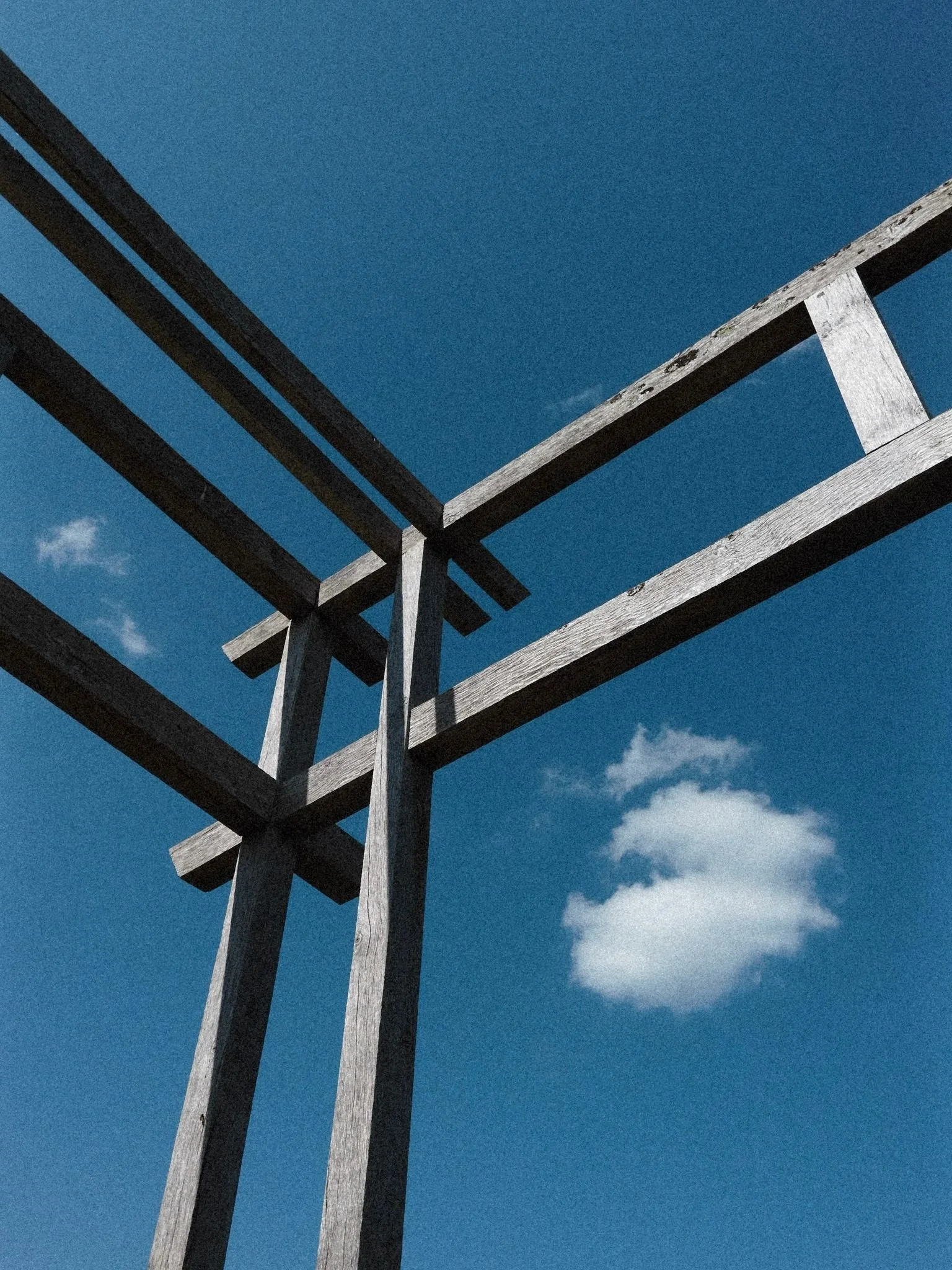 A photograph taken from below of a wooden structure against a blue sky with a few white clouds.