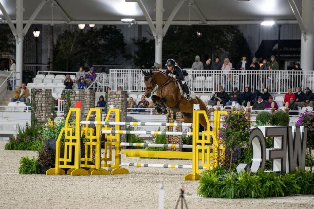Bryn Sadler riding Catch the Dollar over a triple bar in the WEC Grand Prix at night with a large crowd in Ocala, Florida