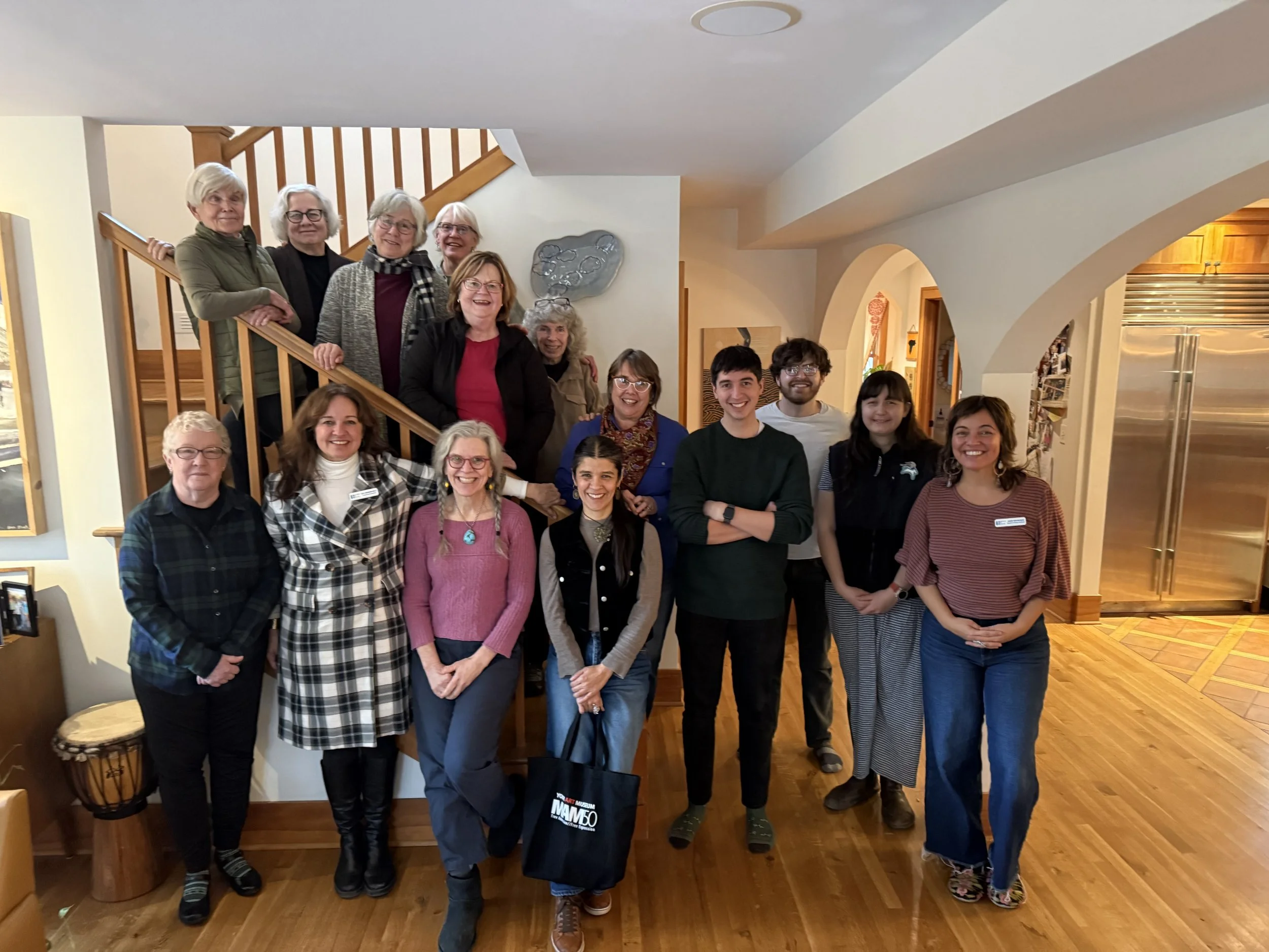 A group of Missoula Art Museum staff, docents, and artists pose together in front of a staircase.
