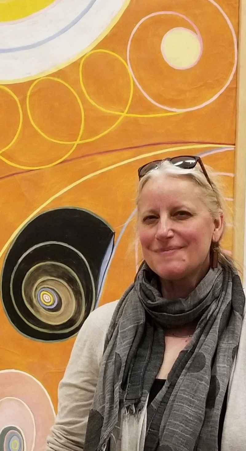 A person smiling in front of an abstract, colorful mural with circular patterns and swirls.