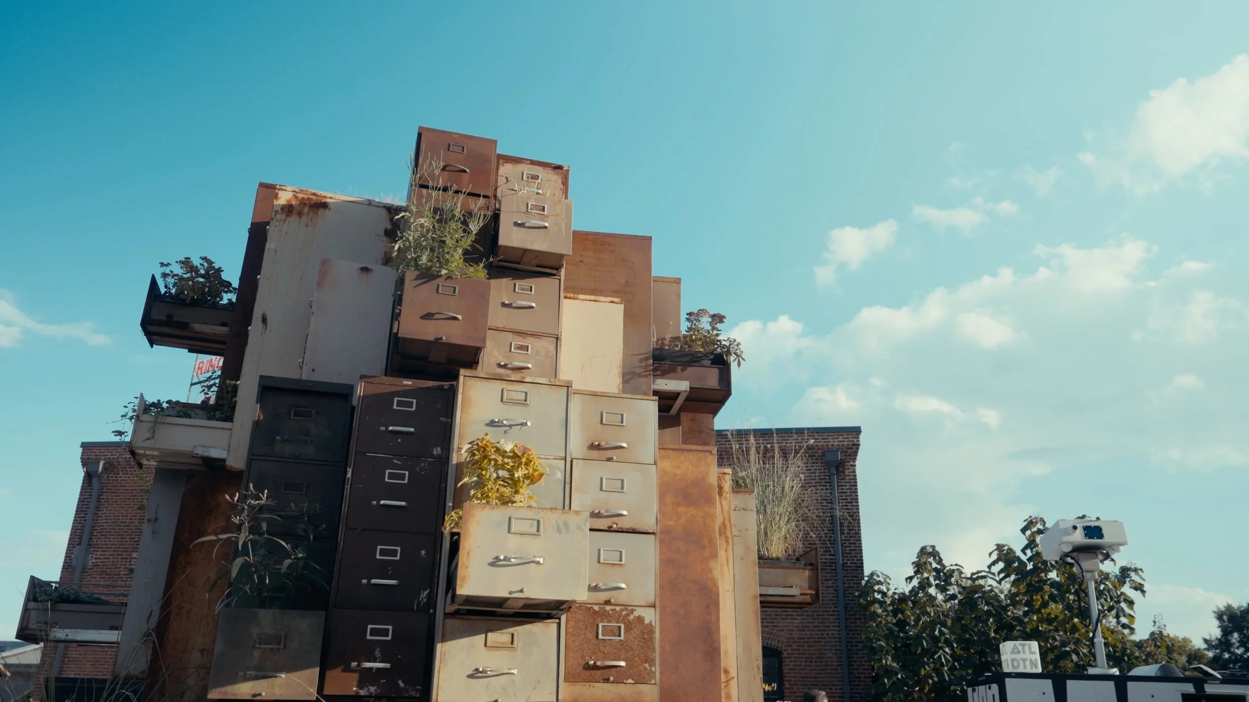 A building with a unique exterior covered in a variety of colorful and weathered mailbox doors, set against a bright blue sky with scattered clouds.