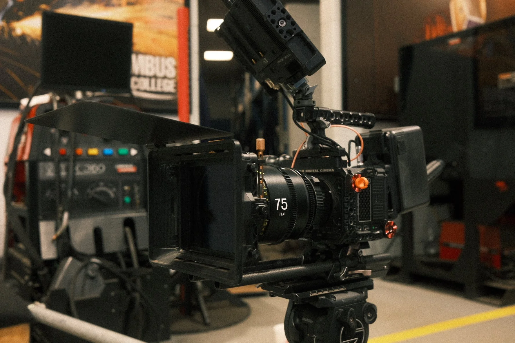 A professional digital cinema camera mounted on a stabilizer rig in a film or TV production set with equipment and storage in the background.