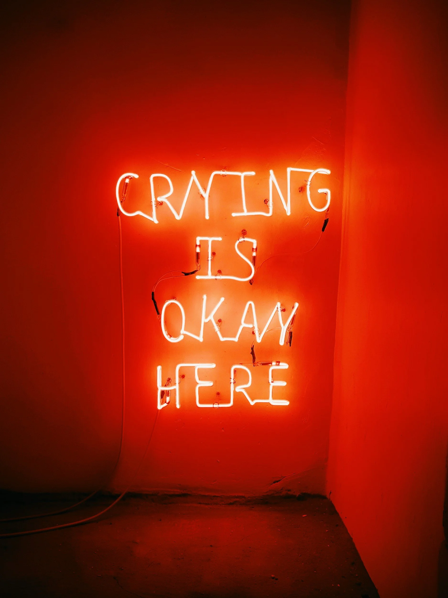 Neon sign on a wall that reads 'Crying is okay here' in bright red and white lights.