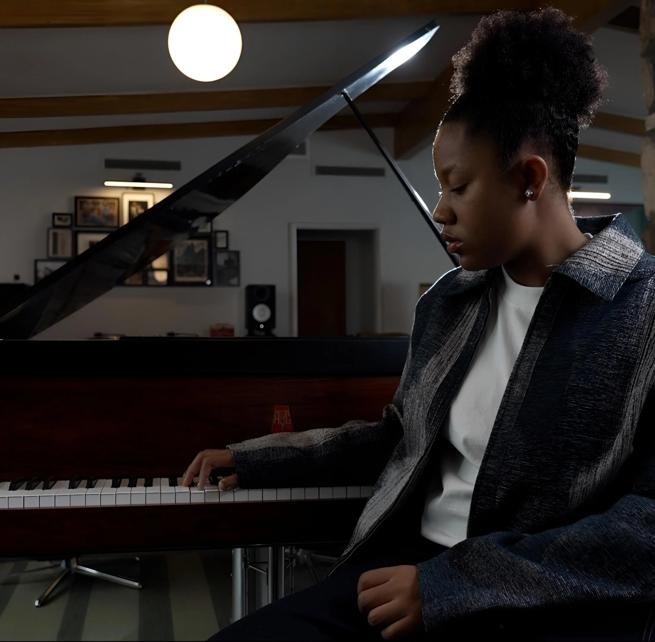 A young woman with natural hair and earrings playing a grand piano in a music studio or room.