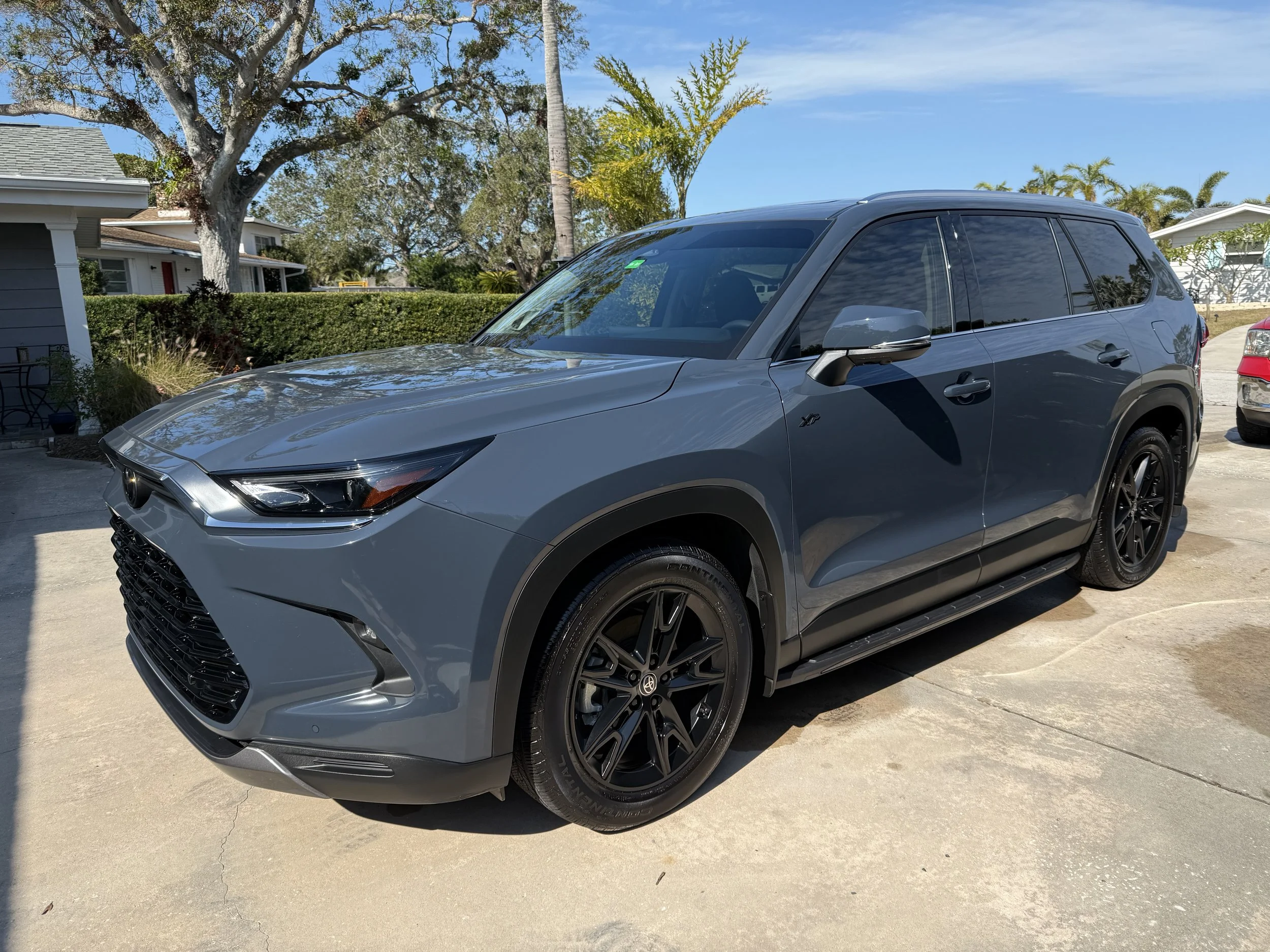 Gray SUV parked on a driveway in front of houses with trees and blue sky in the background.