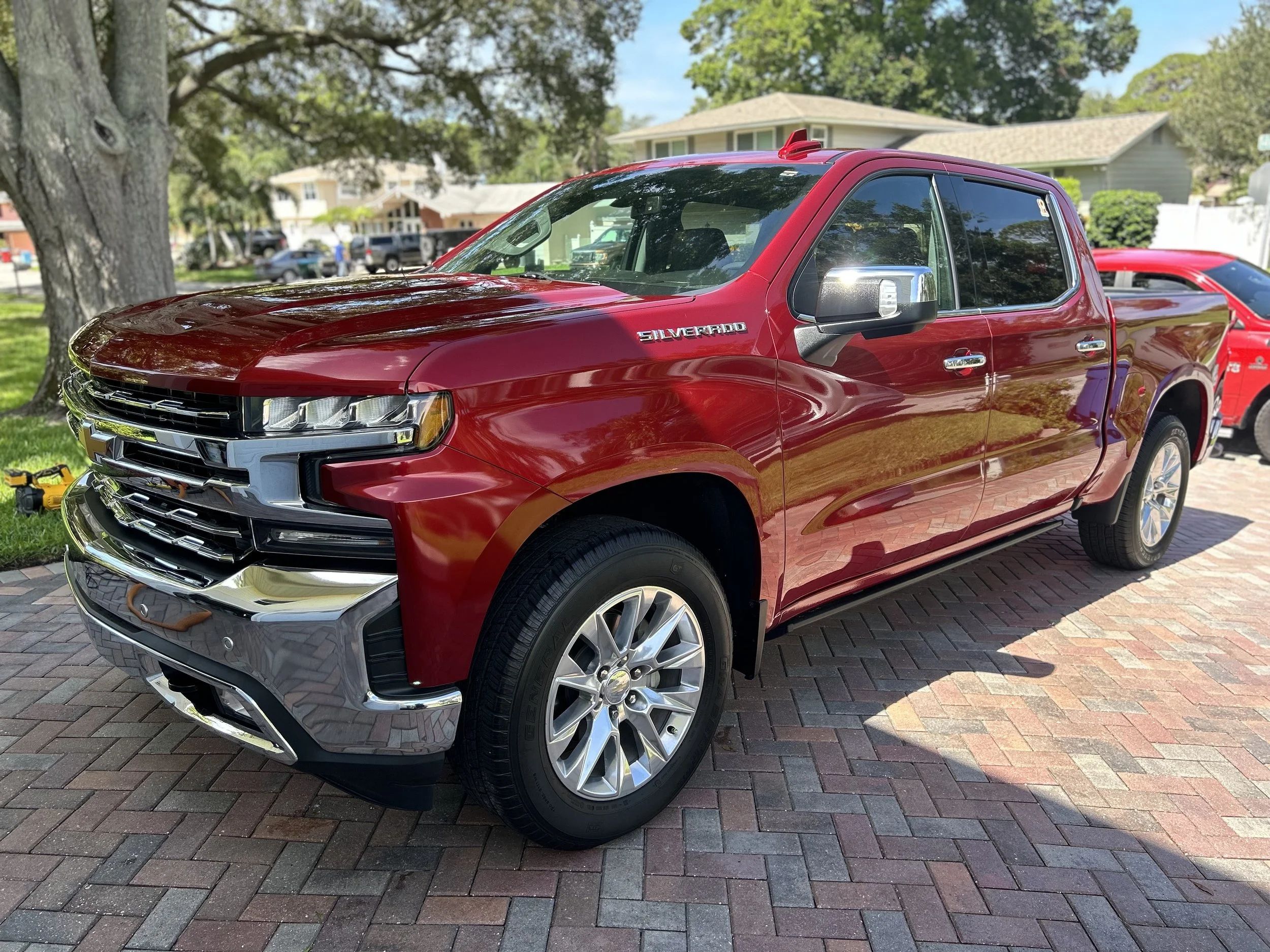 Red Chevrolet Silverado pickup truck parked on brick driveway in residential area with trees and houses in the background.