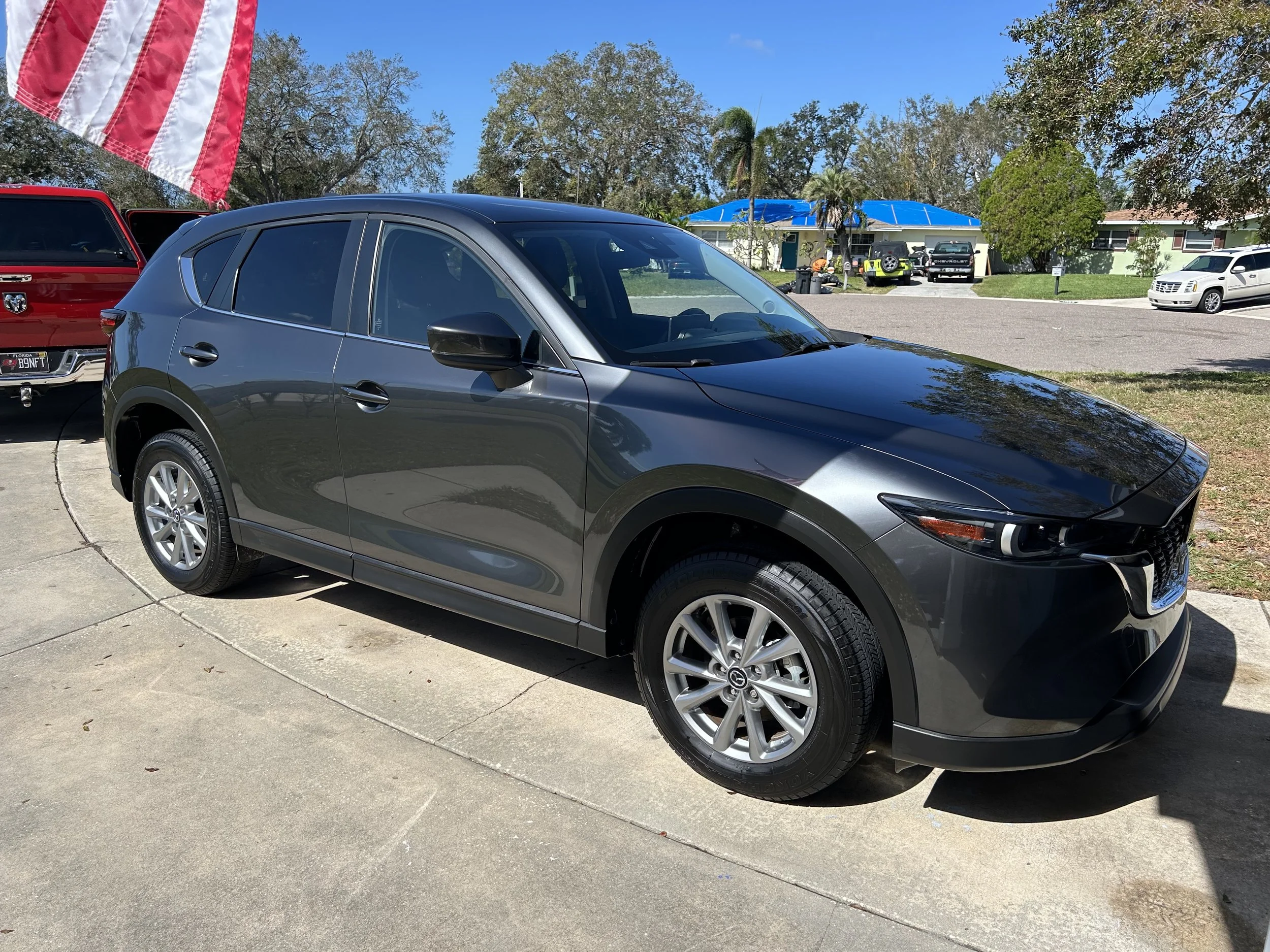 Gray compact SUV parked on a driveway with an American flag on the left and a suburban neighborhood in the background.