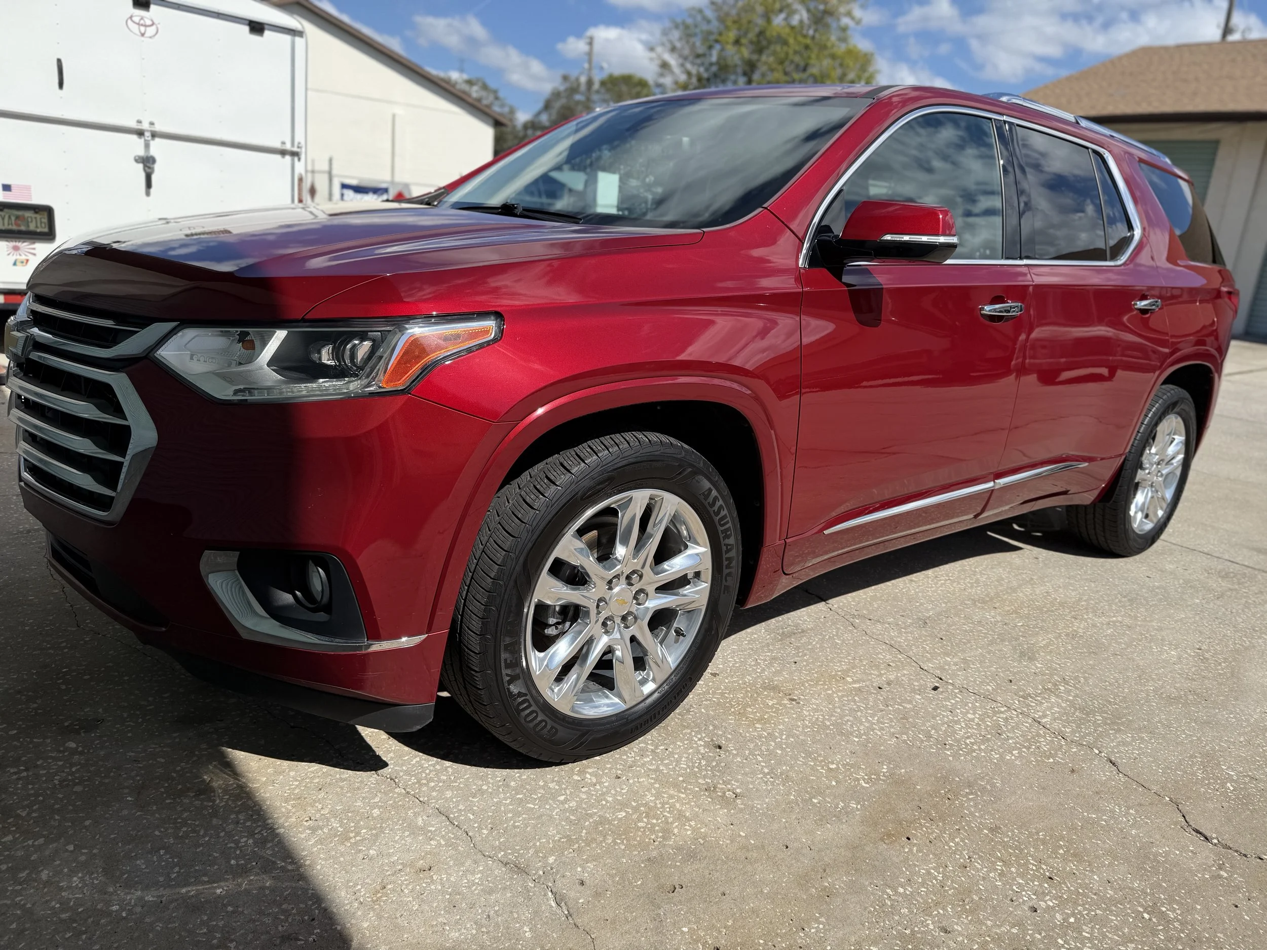 Red SUV parked on a concrete driveway with a white garage and buildings in the background.