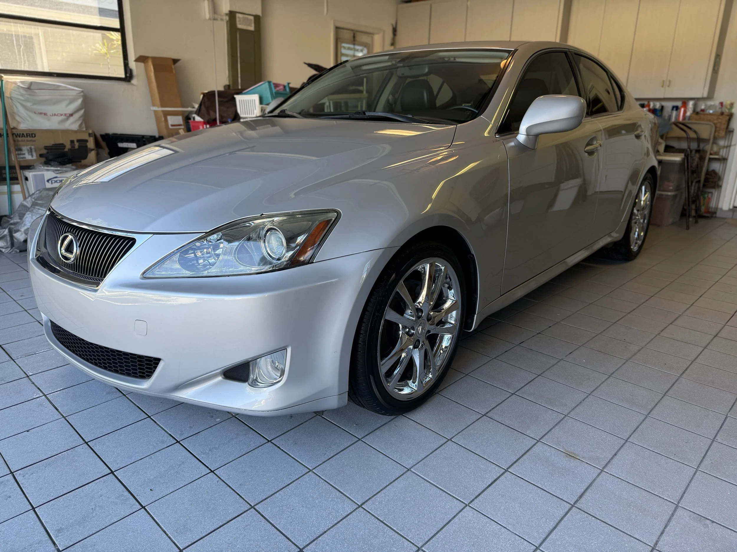 A silver Lexus sedan parked inside a garage with cluttered storage items in the background.