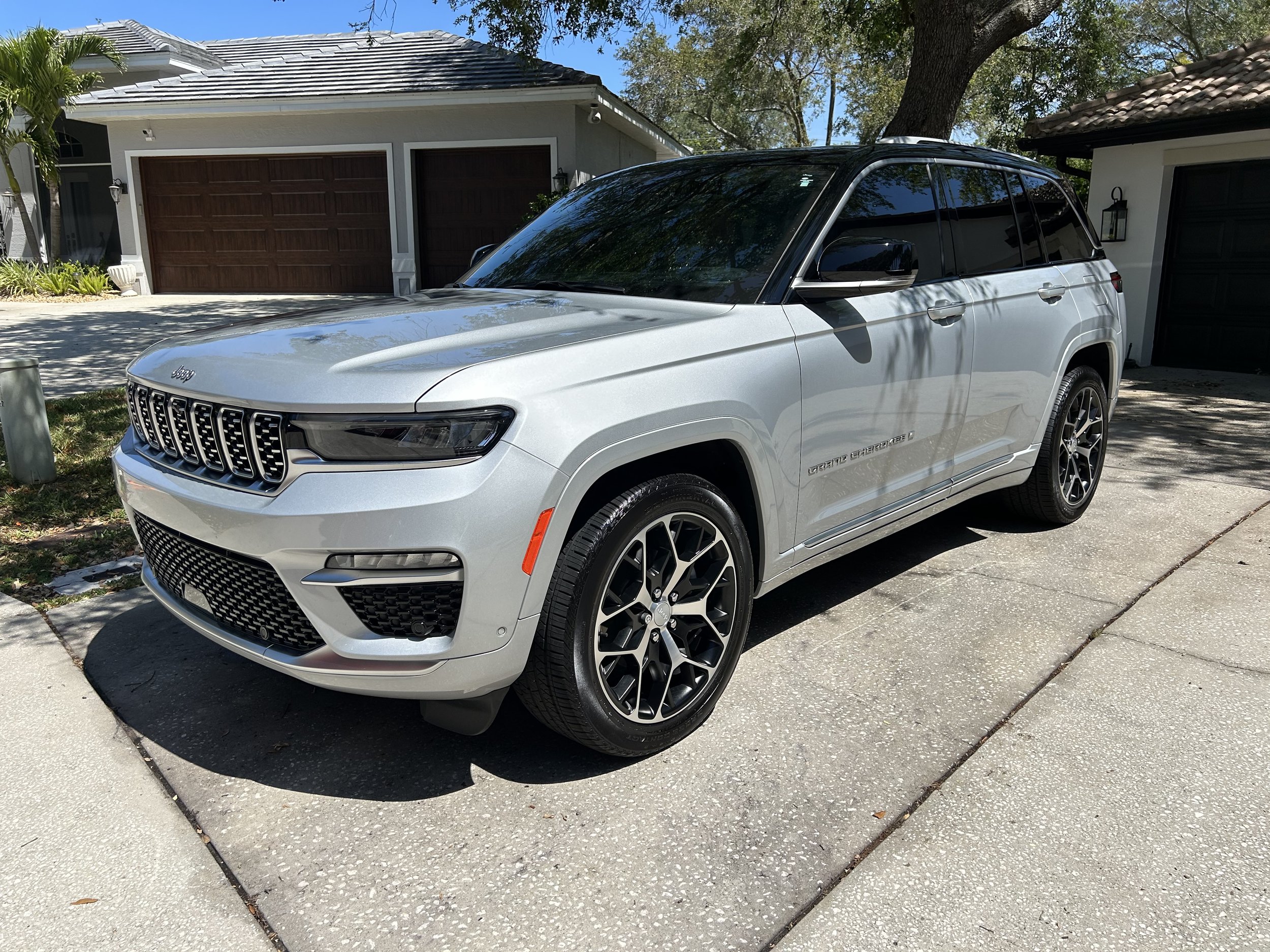 A silver Jeep SUV parked on a driveway in front of a house with a two-car garage and some trees.