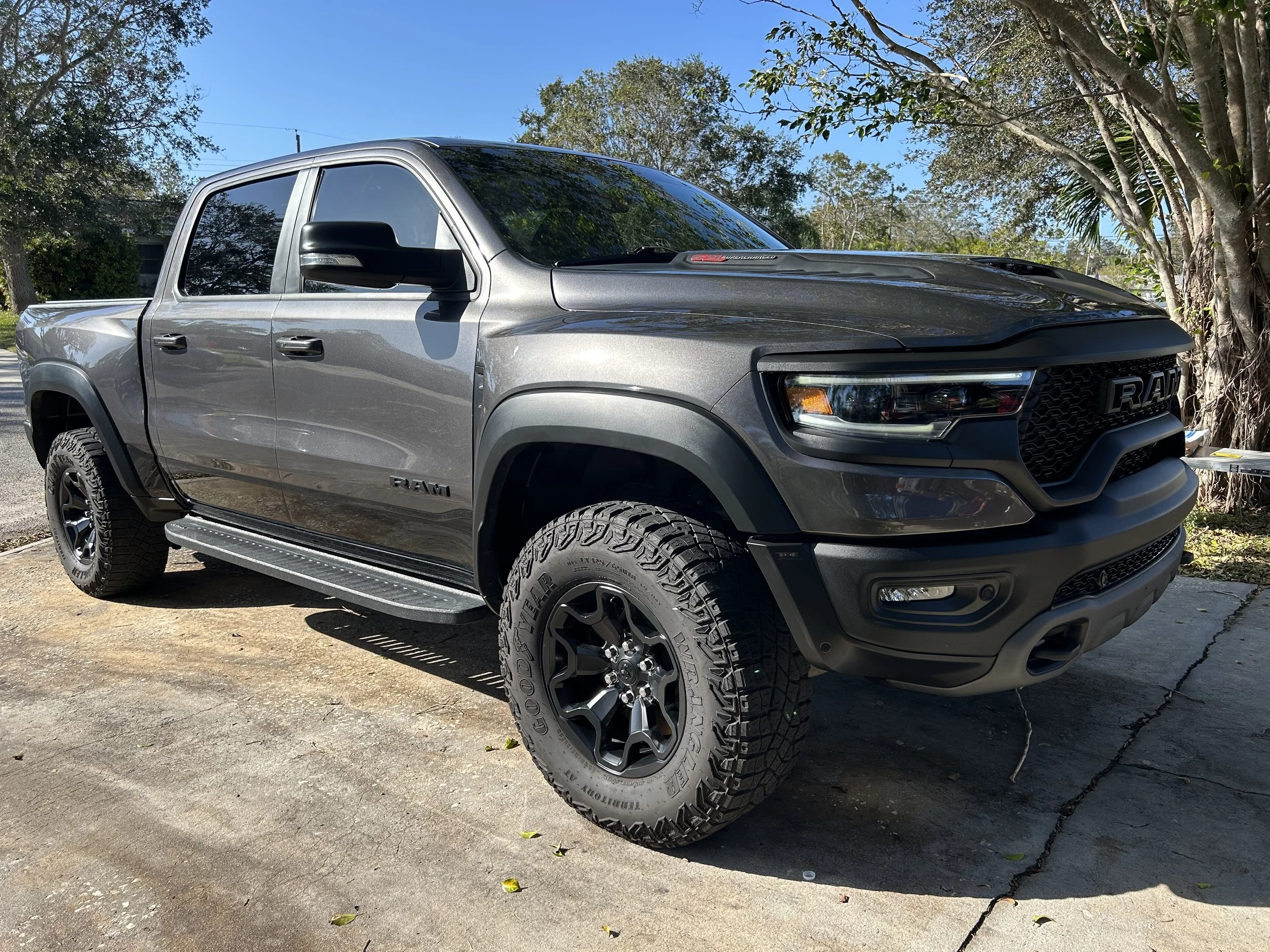 A grey RAM pickup truck parked on a concrete surface with trees and blue sky in the background.