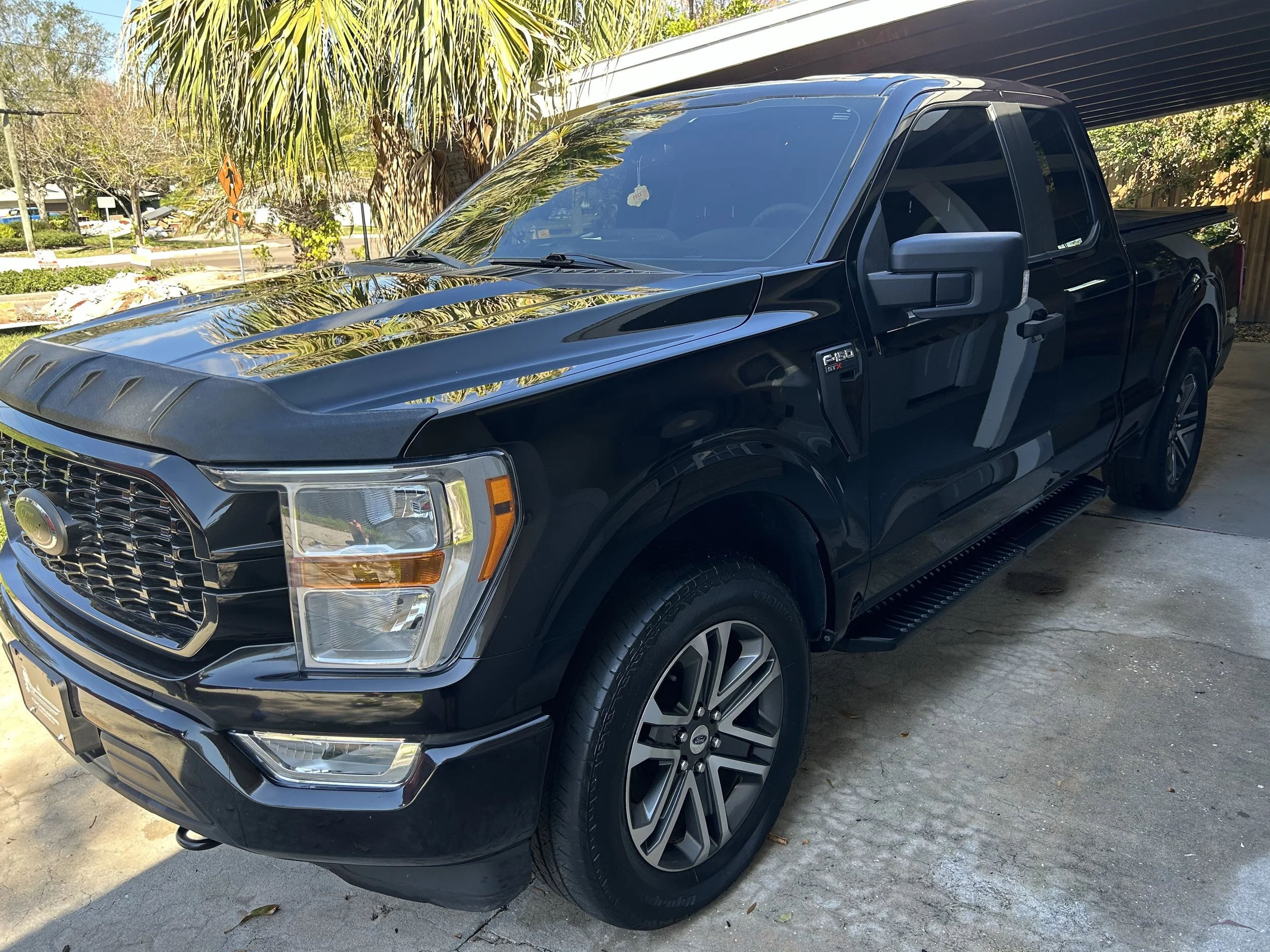 Black Ford F-150 pickup truck parked in a driveway with trees and a house in the background.