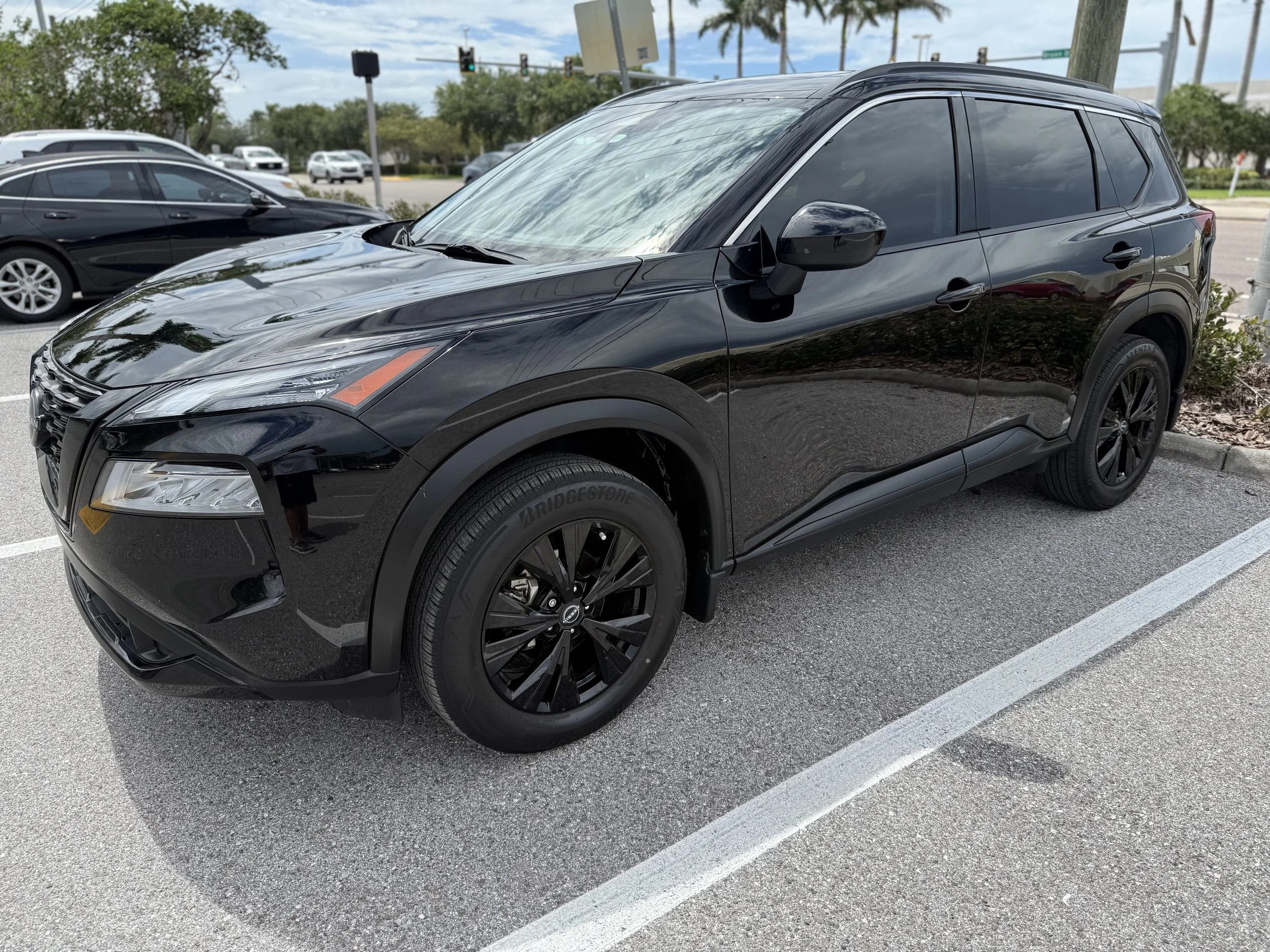 Black SUV parked in a parking lot with other cars and trees in the background.
