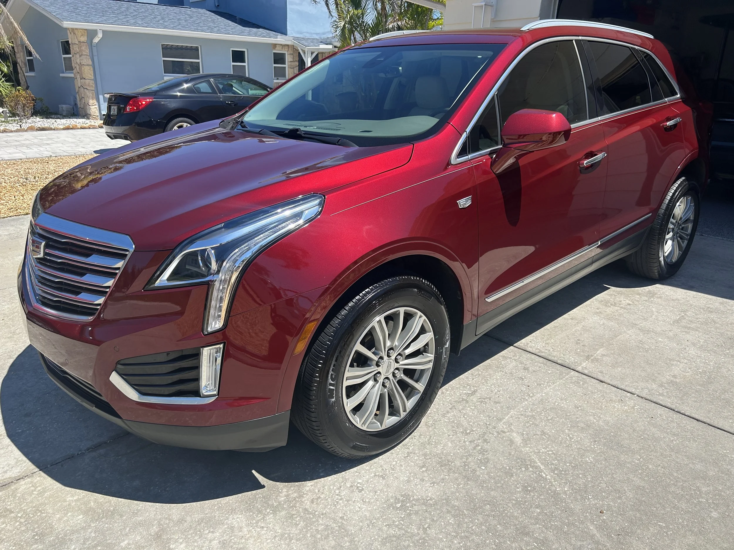 Red luxury SUV car parked on driveway in front of house, with black car parked behind.