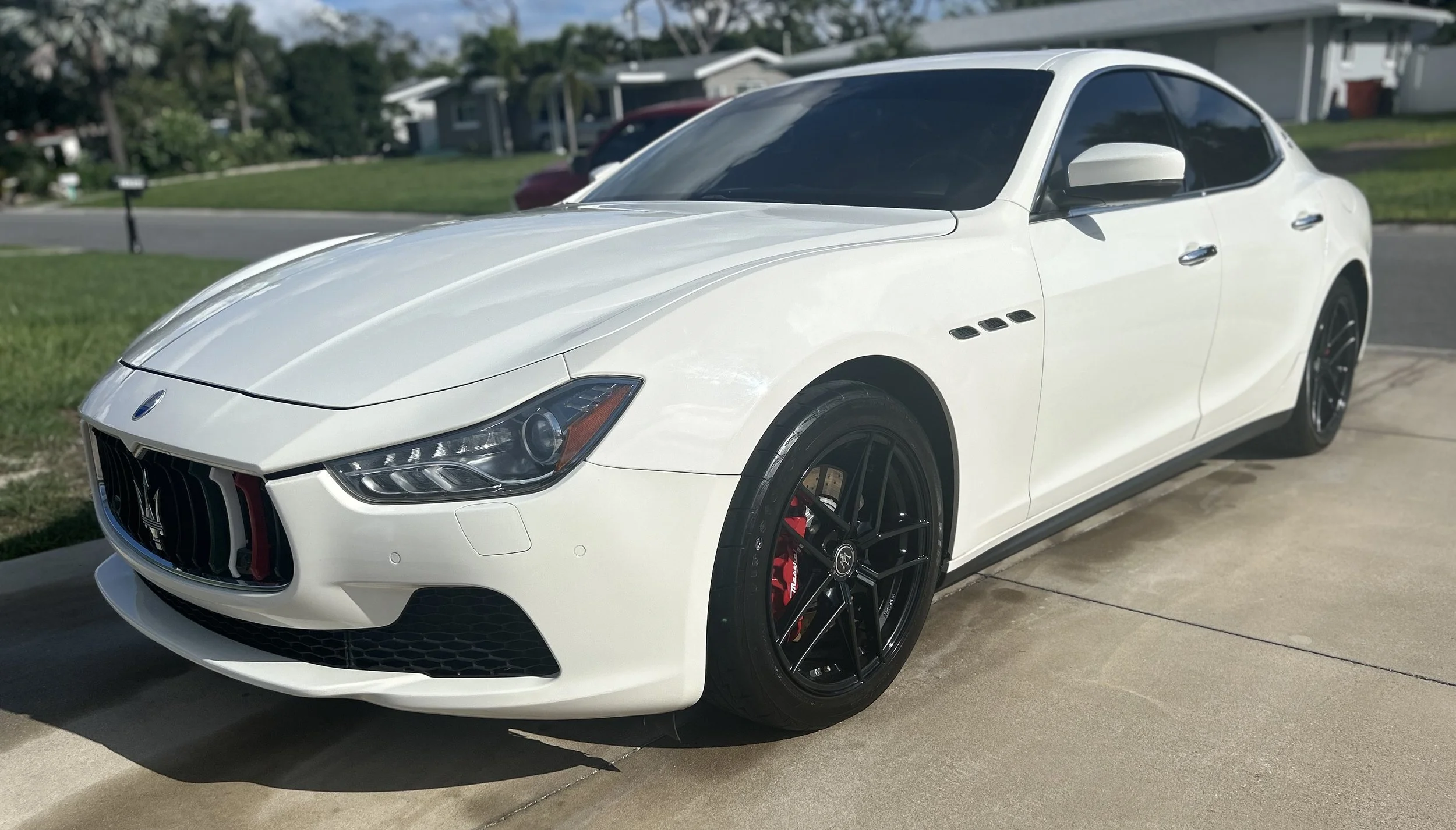 White luxury sports car parked on driveway in a suburban neighborhood.