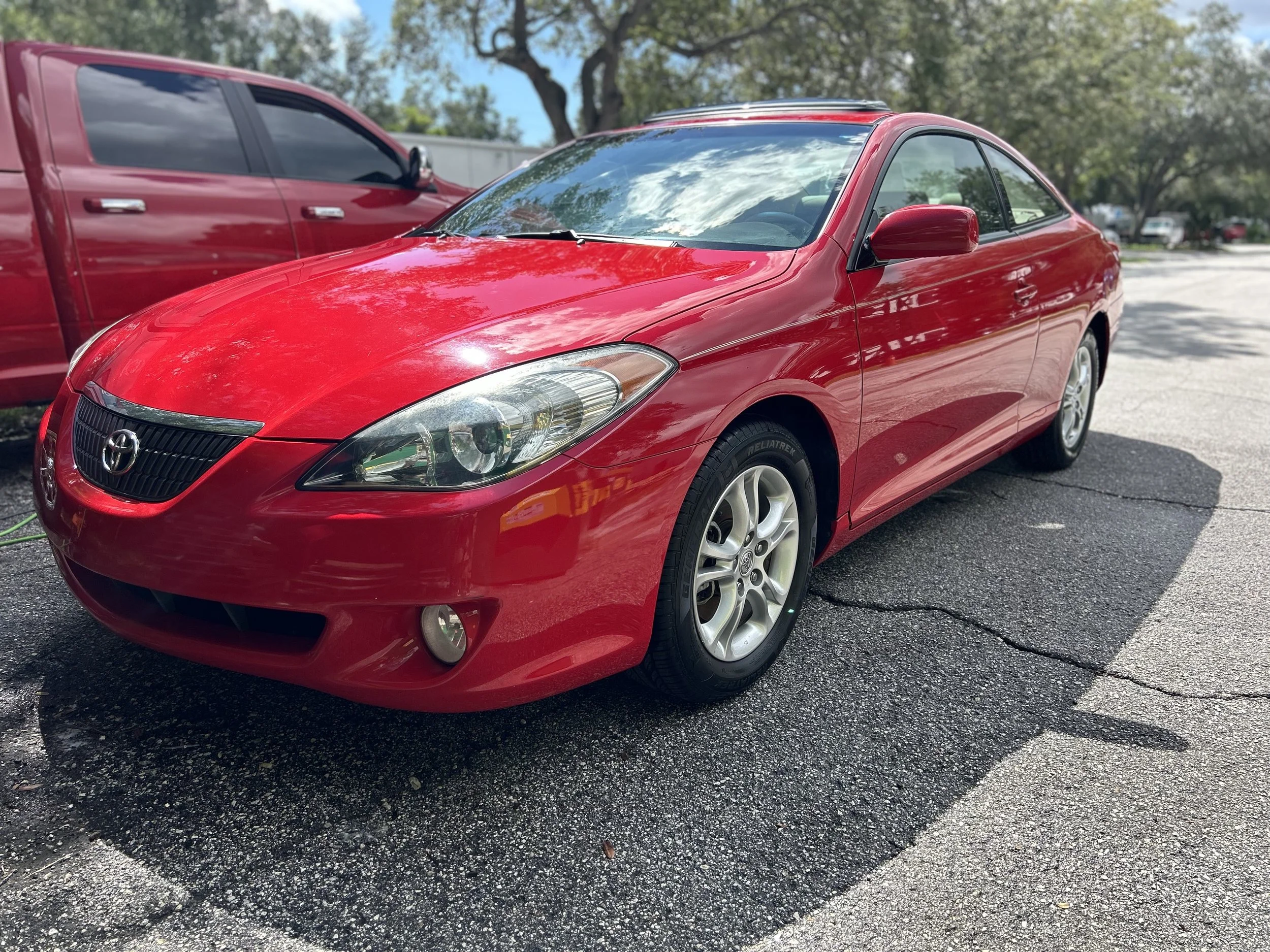 Red Toyota Solara parked on a paved lot with a tree and blue sky in the background.
