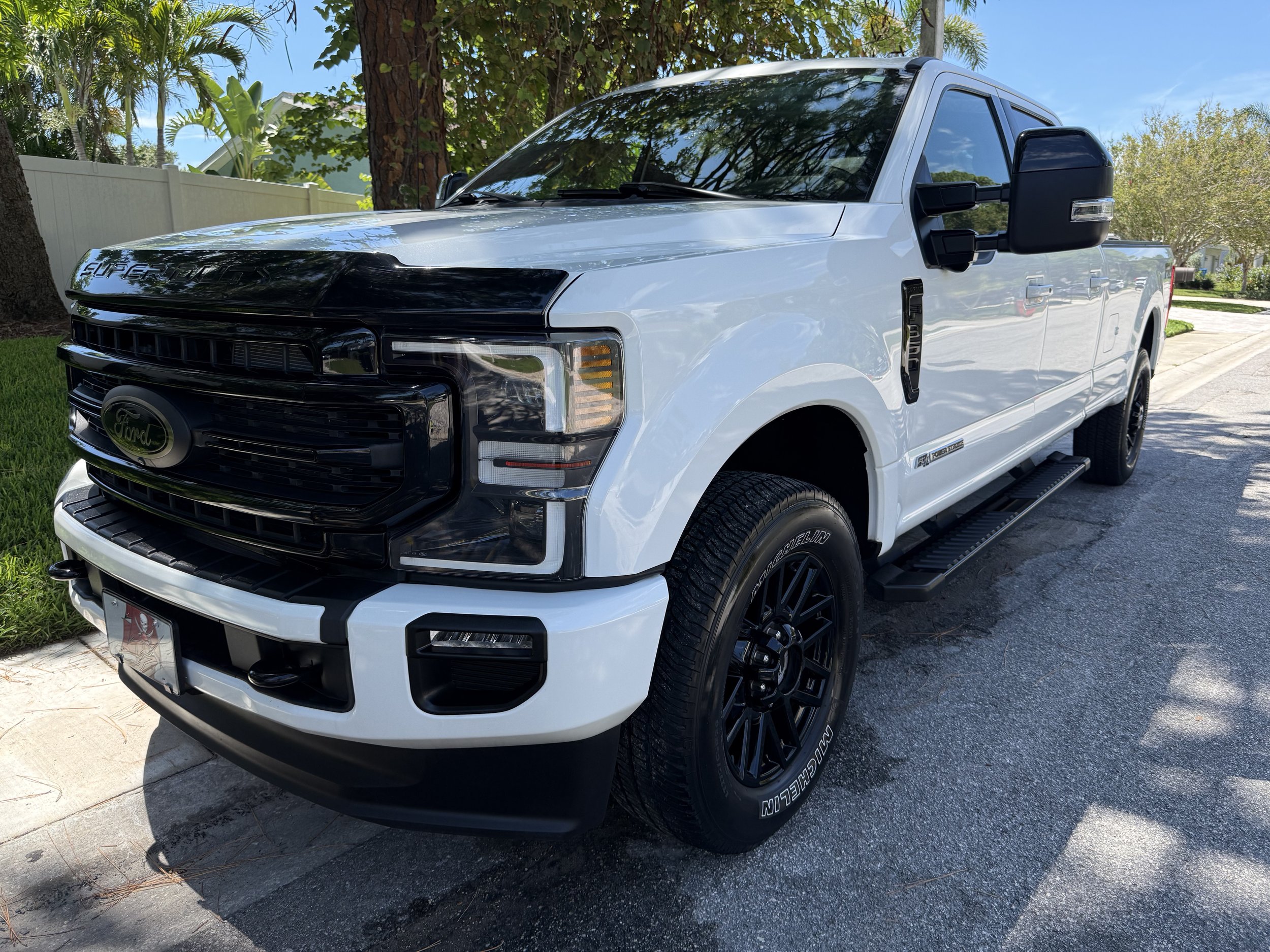 A white Ford F-250 Super Duty pickup truck parked on a suburban street under trees.