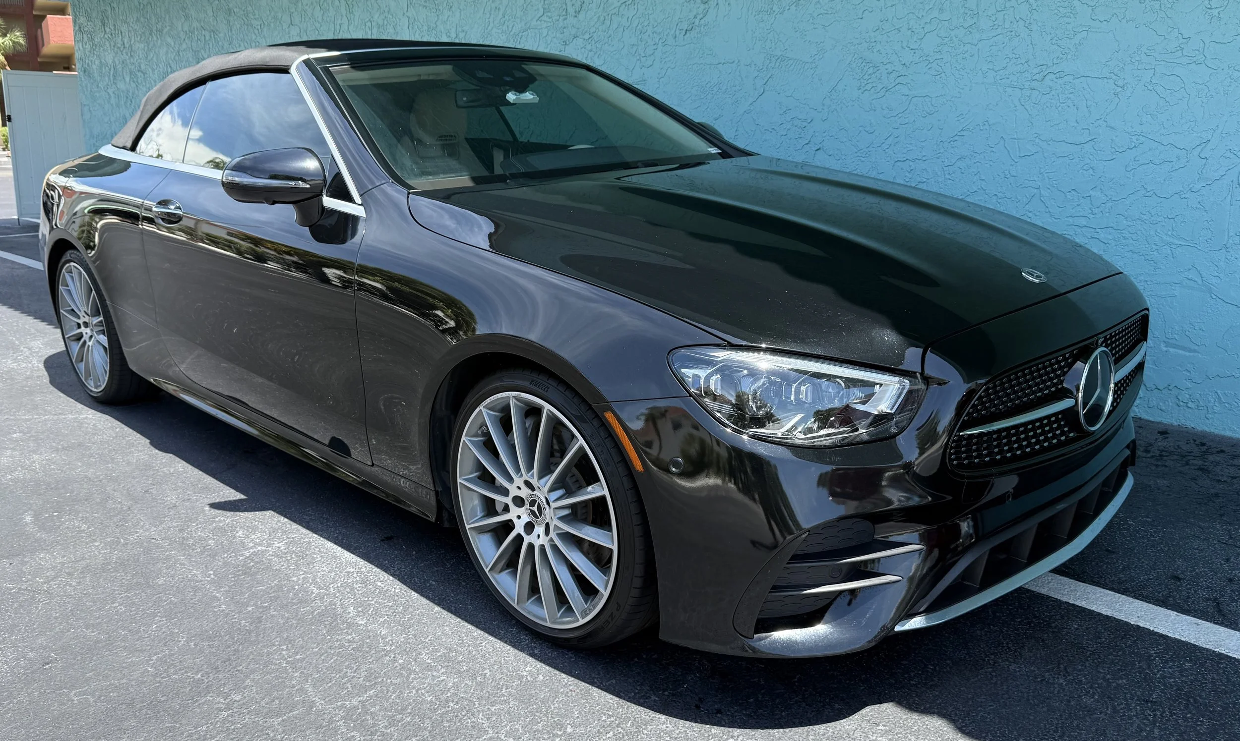 Black Mercedes-Benz convertible car parked on asphalt near a turquoise wall
