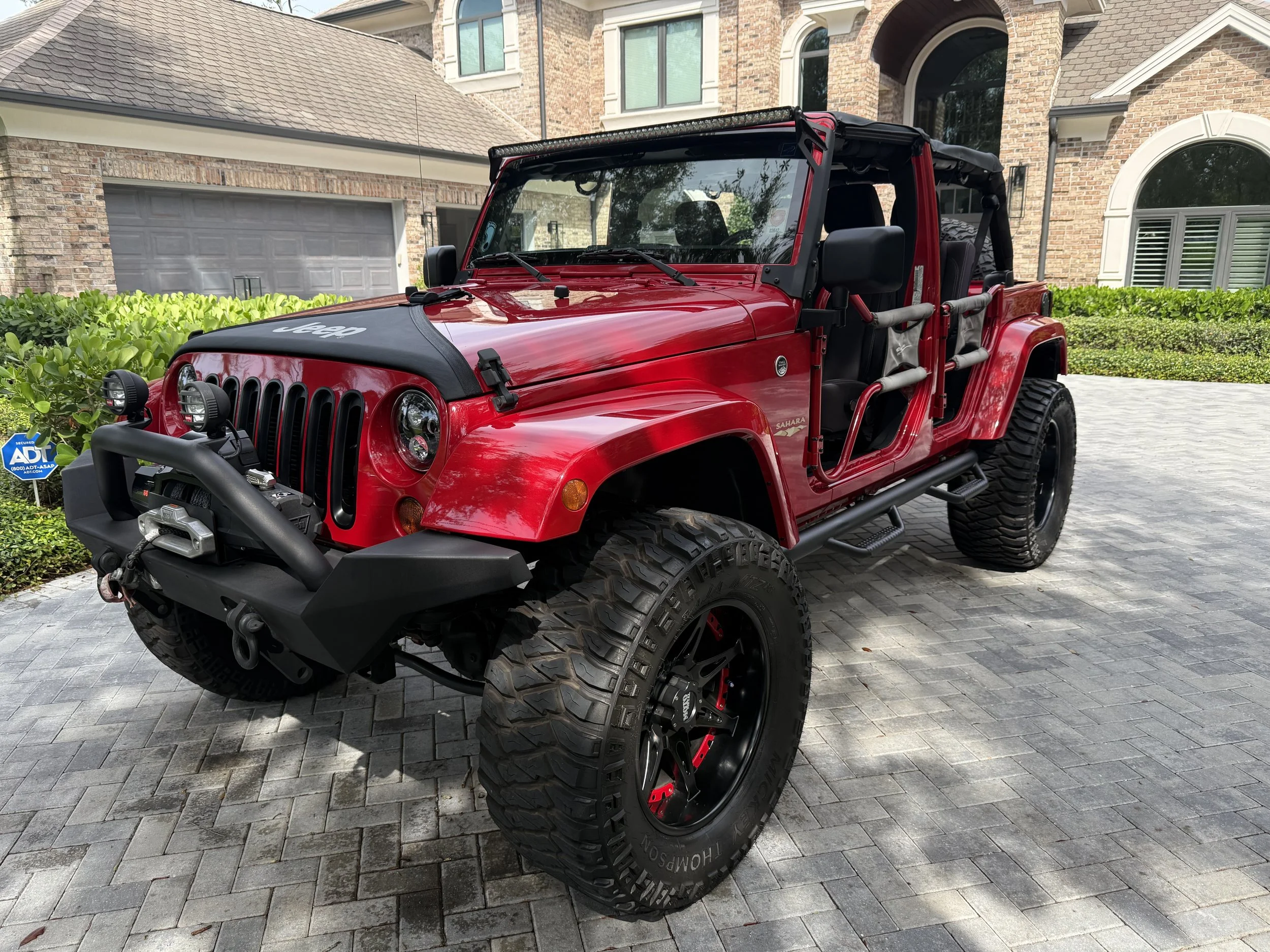 Red Jeep Wrangler with black accents parked on a driveway in front of a house.