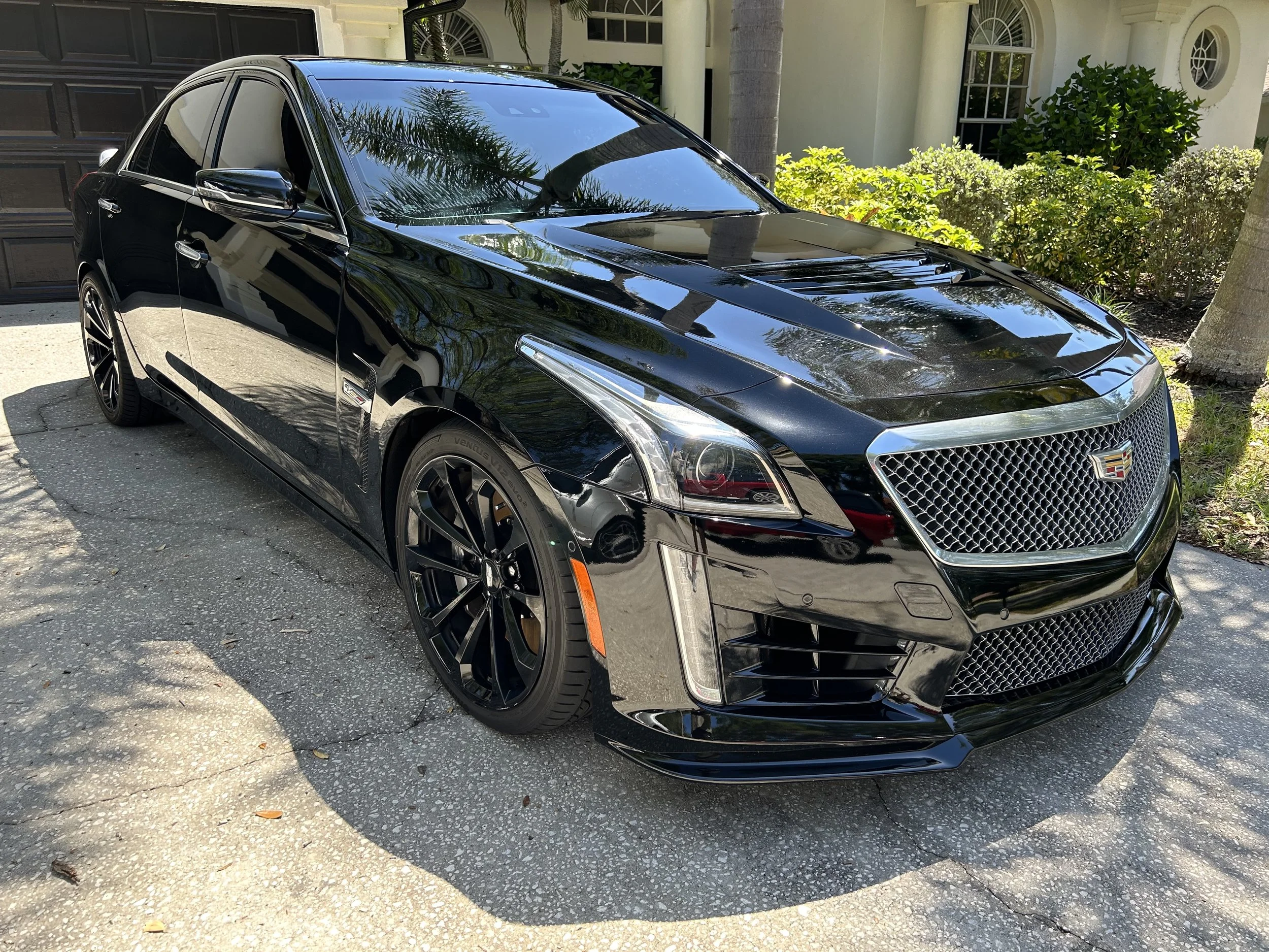Black Cadillac sedan parked outside on a driveway, reflecting trees and sky on its shiny surface.