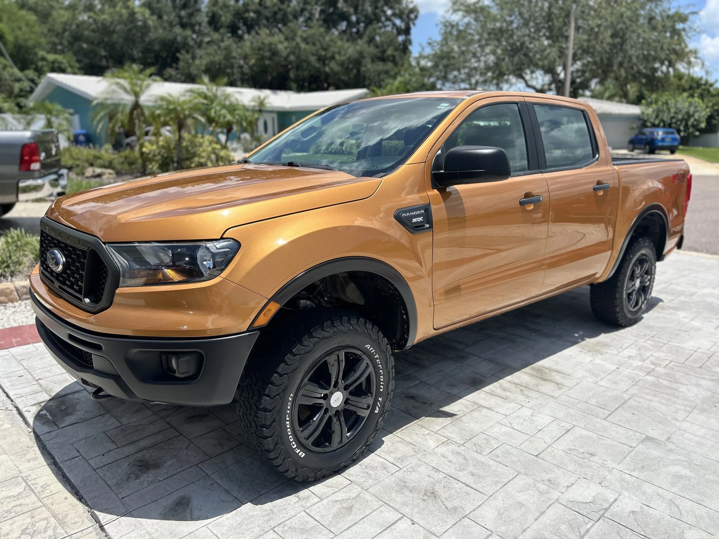 Orange Ford Ranger pickup truck parked on a driveway with a house and greenery in the background.