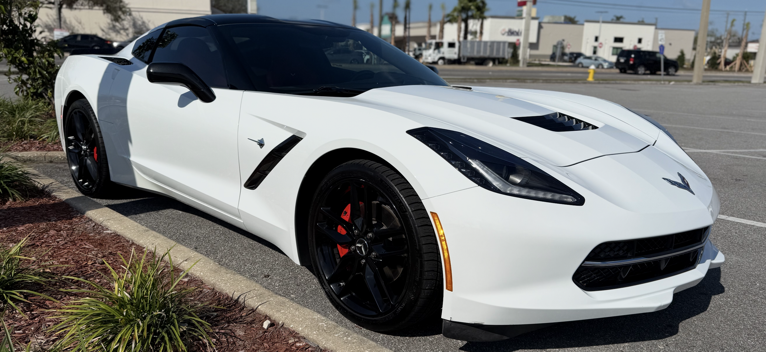 A white Chevrolet Corvette sports car with black wheels and red brake calipers parked in a parking lot.