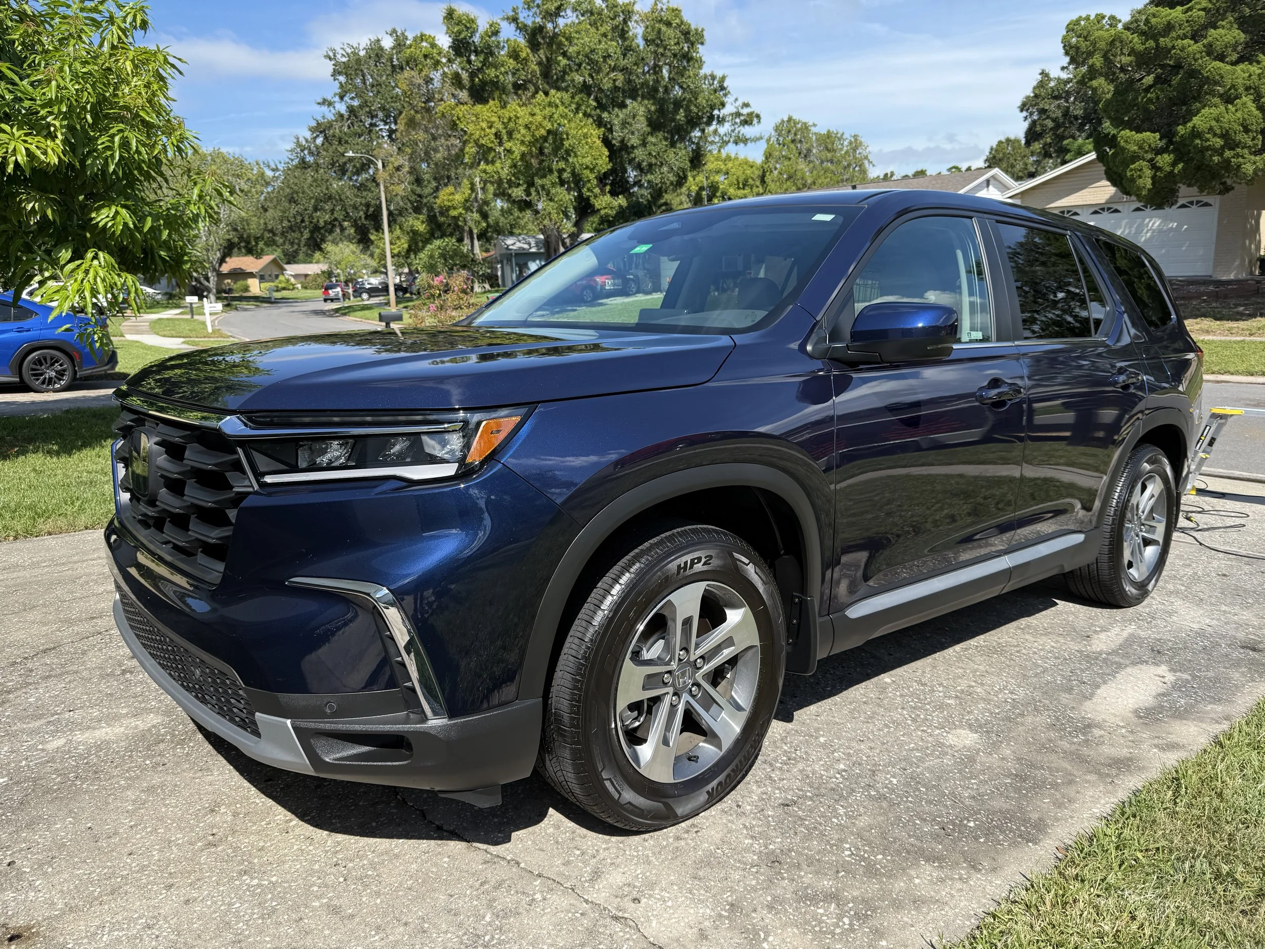 A dark blue SUV parked on a driveway in a residential neighborhood, with trees and houses in the background.