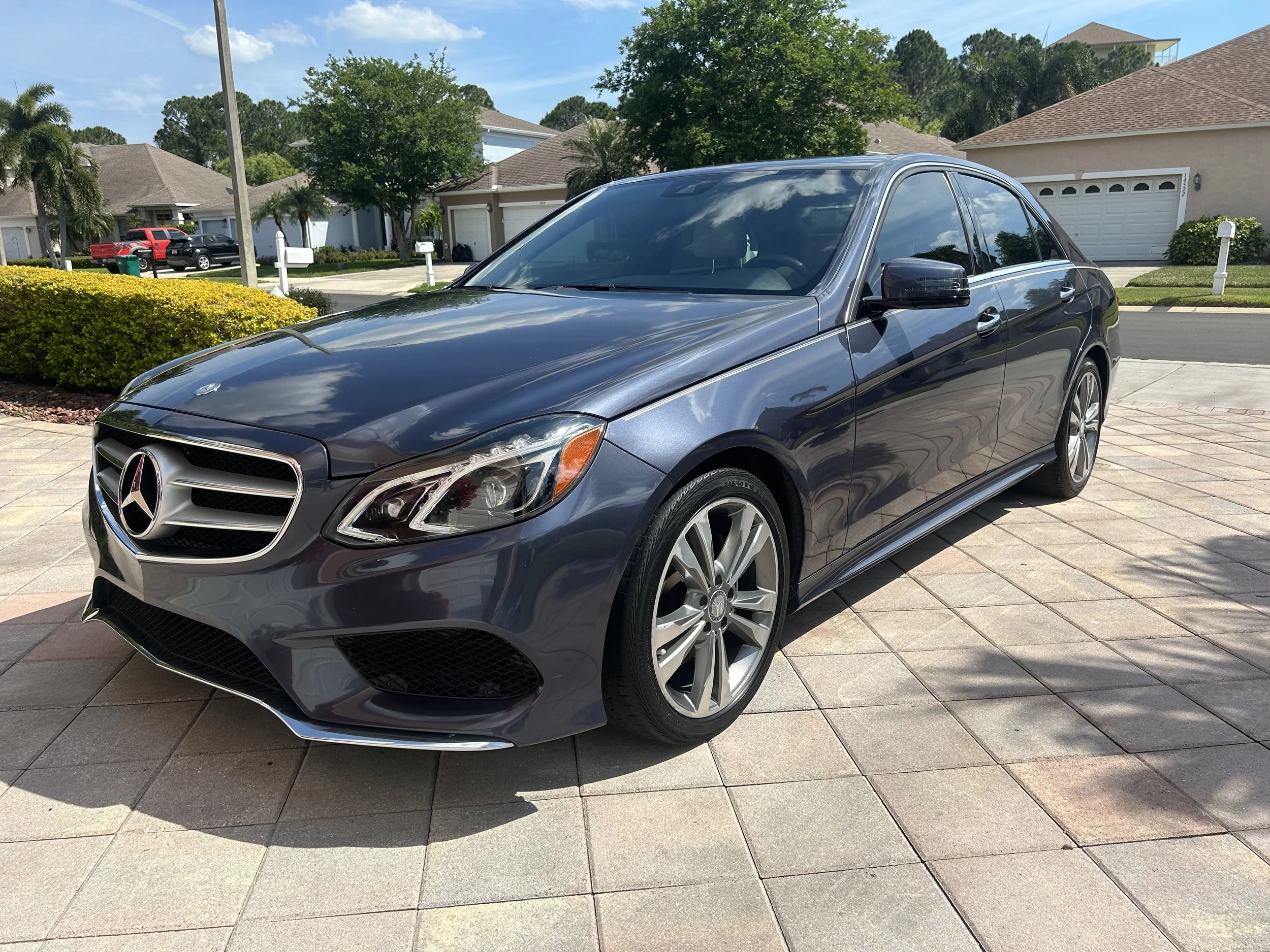 Blue Mercedes-Benz sedan parked on a driveway with houses and trees in the background.