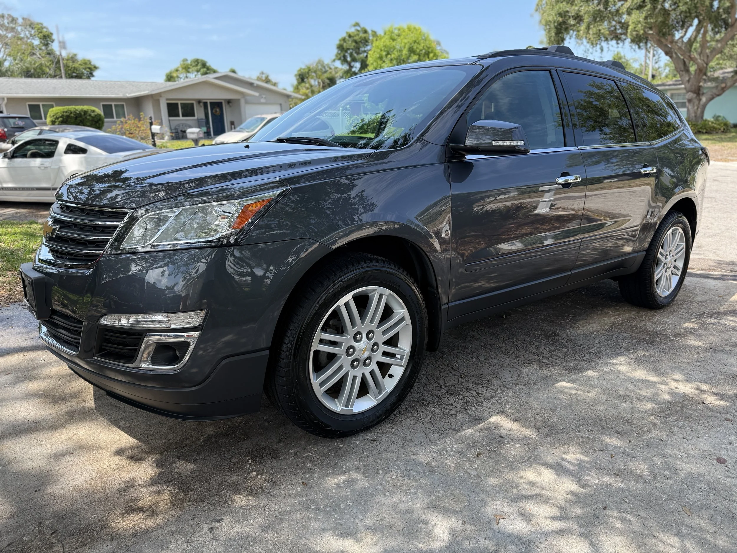A black Chevrolet Traverse SUV parked on a driveway with houses and trees in the background.