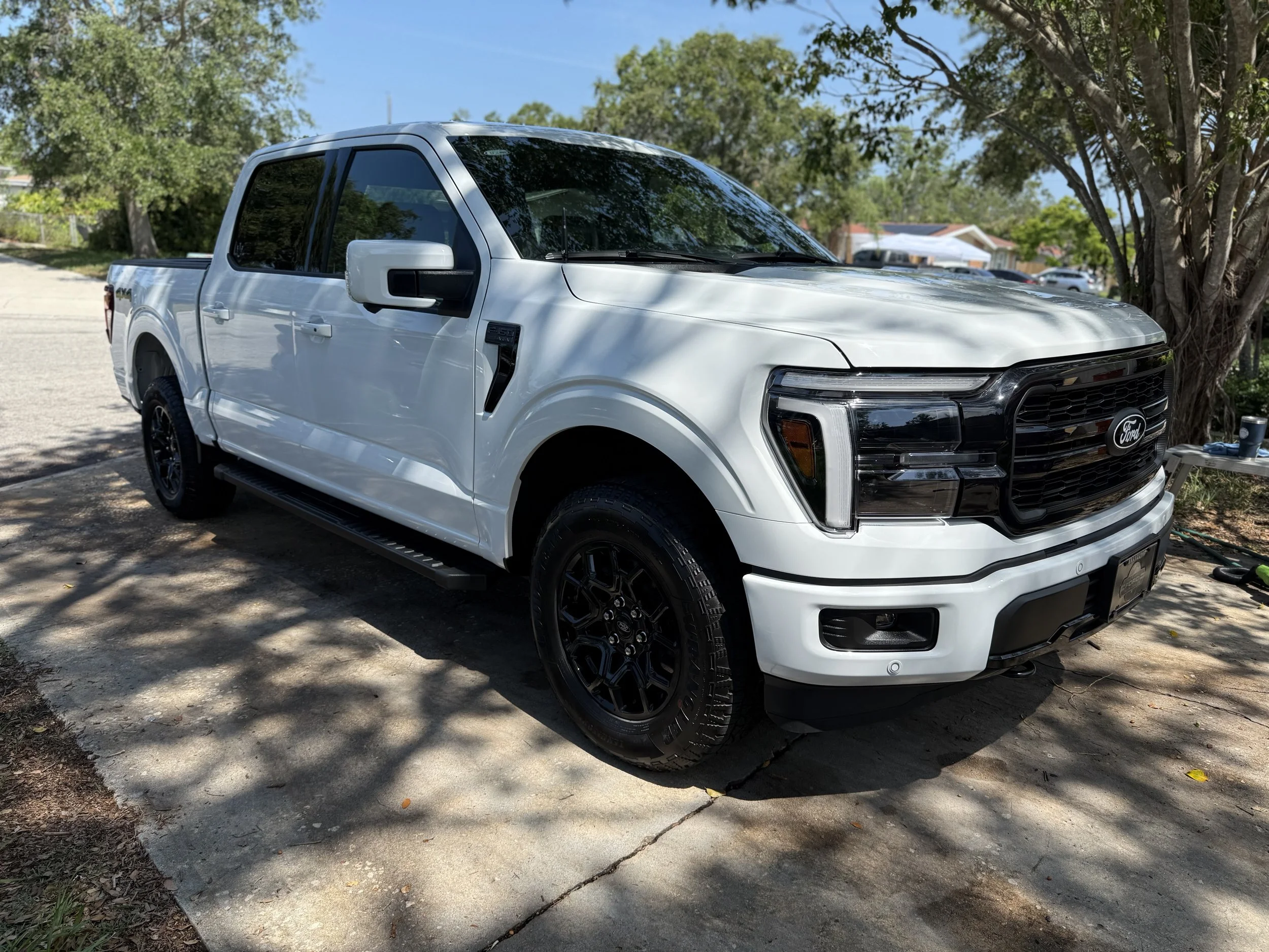 White Ford pickup truck parked on a driveway in a shaded area with trees and houses in the background.