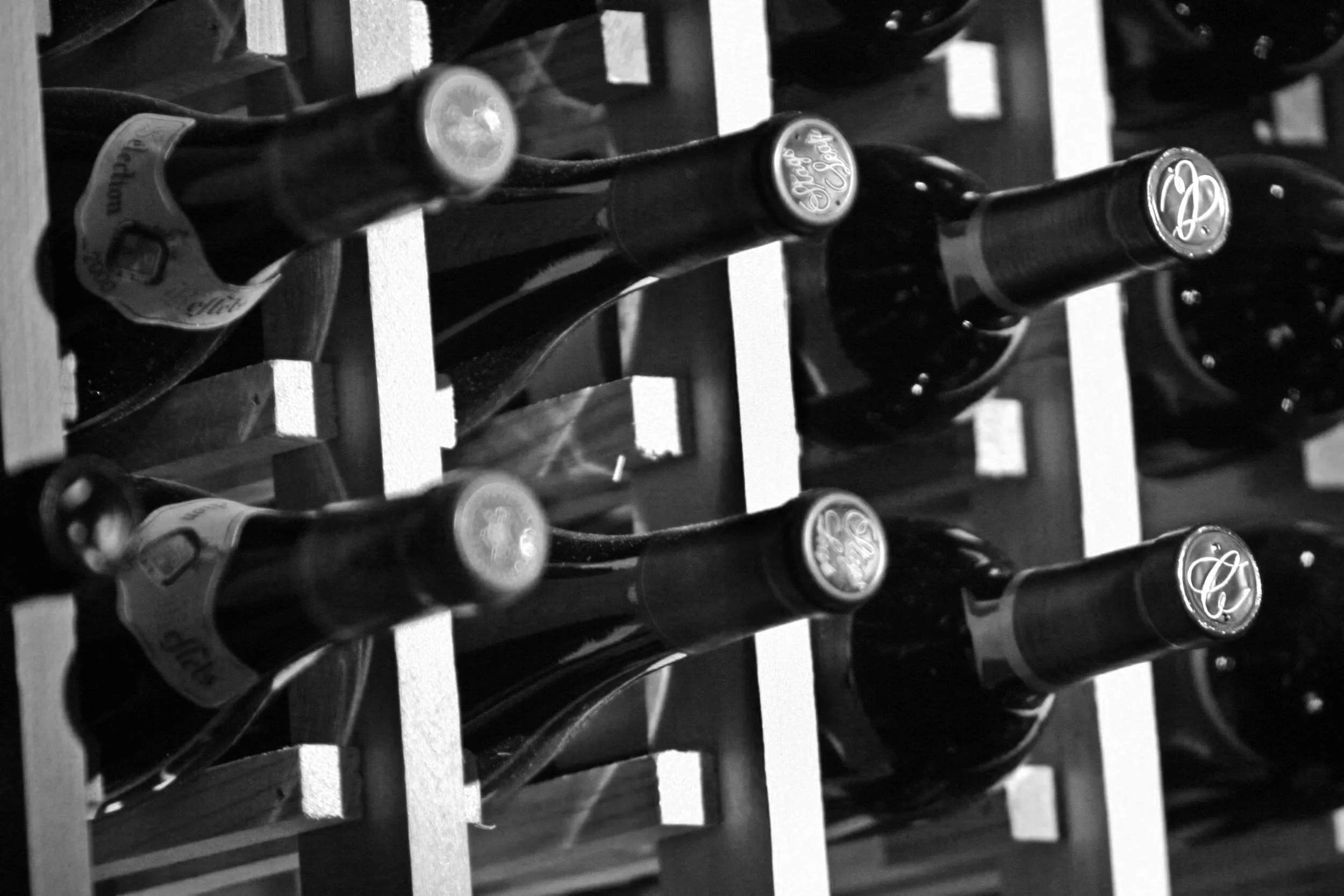 Multiple bottles of beer stored on a wine rack, viewed from above in black and white.