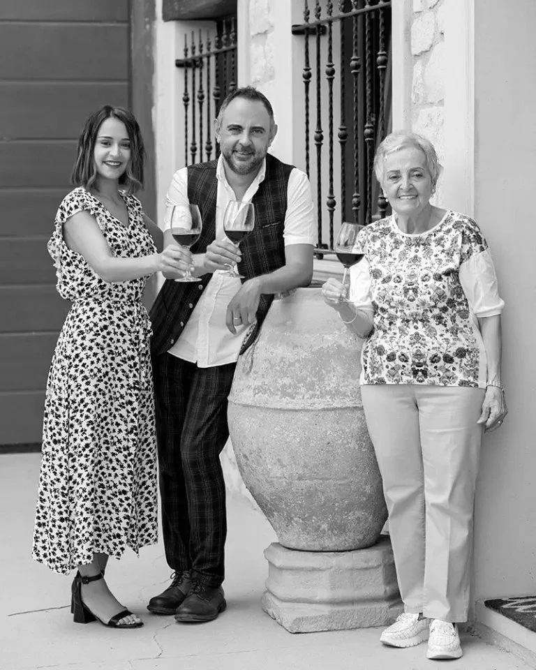 Three people standing outside, holding glasses of red wine, smiling at the camera.