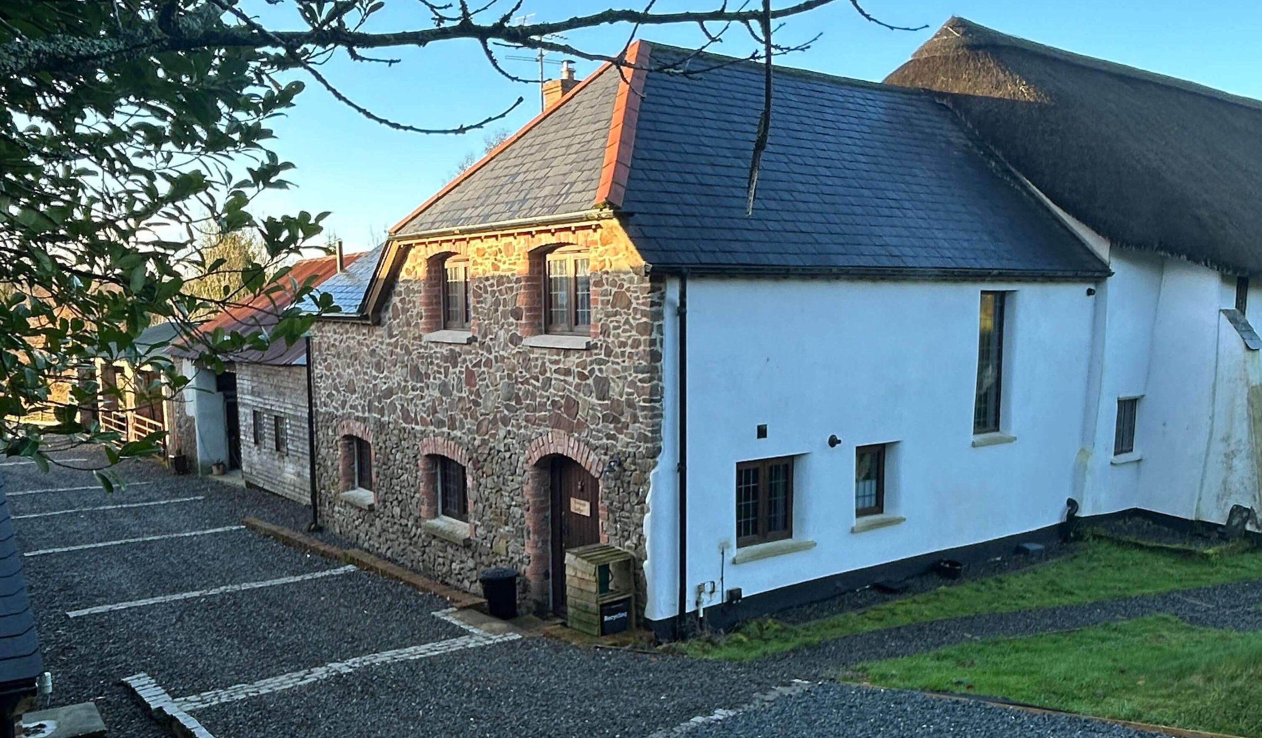 Keepers Lodge has stone and cob walls facade with white exterior on the side, featuring a slate roof, multiple windows, and a parking lot in the foreground.