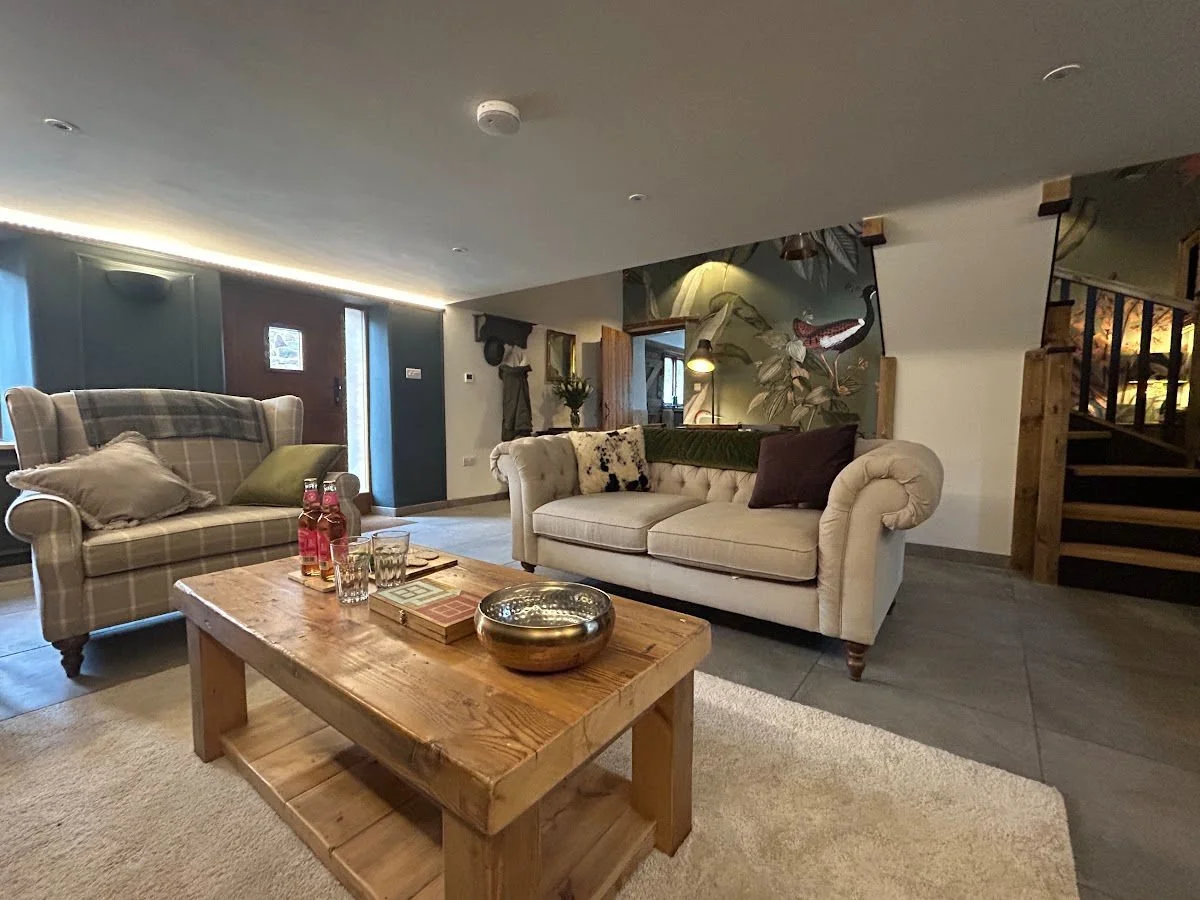 Living room with two sofas, wooden coffee table, decorative pillows, and a wall mural with a bird and plants, near a staircase.