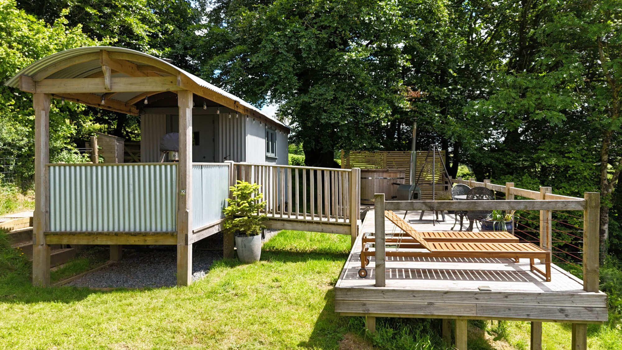 Backyard with a wooden deck, outdoor furniture, potted plants, and a storage shed surrounded by green trees.