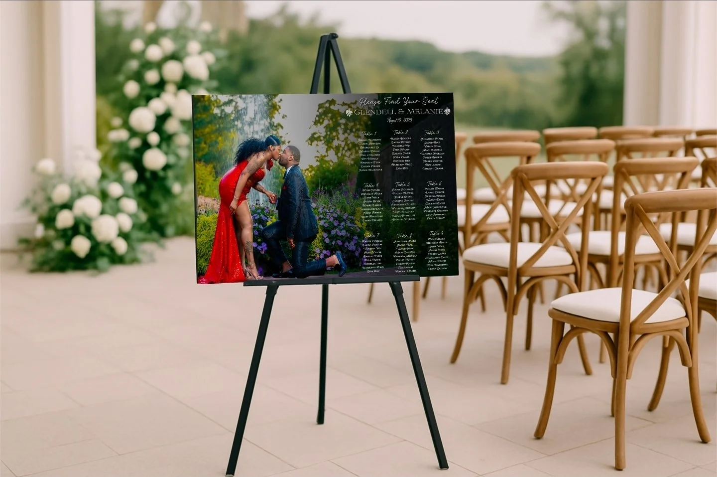 Wedding seating chart display with a couple image, placed on a black easel inside a decorated venue with wooden chairs and landscape view outside.