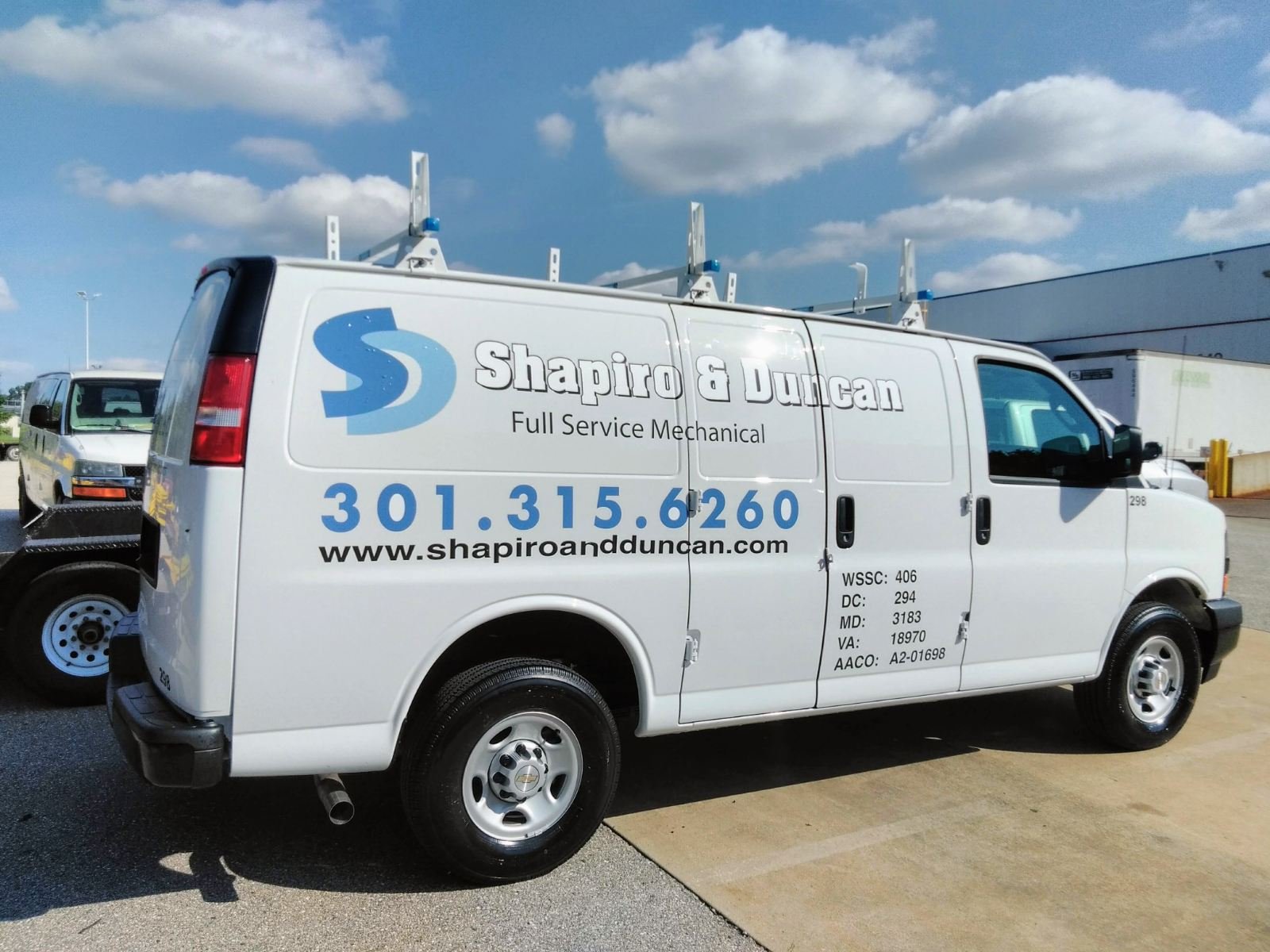 White service van with blue and black lettering for Shapiro & Duncan, a full service mechanical company, with contact number 301-315-6260 and website www.shapiroandduncan.com, parked in a lot with a blue sky and clouds overhead.