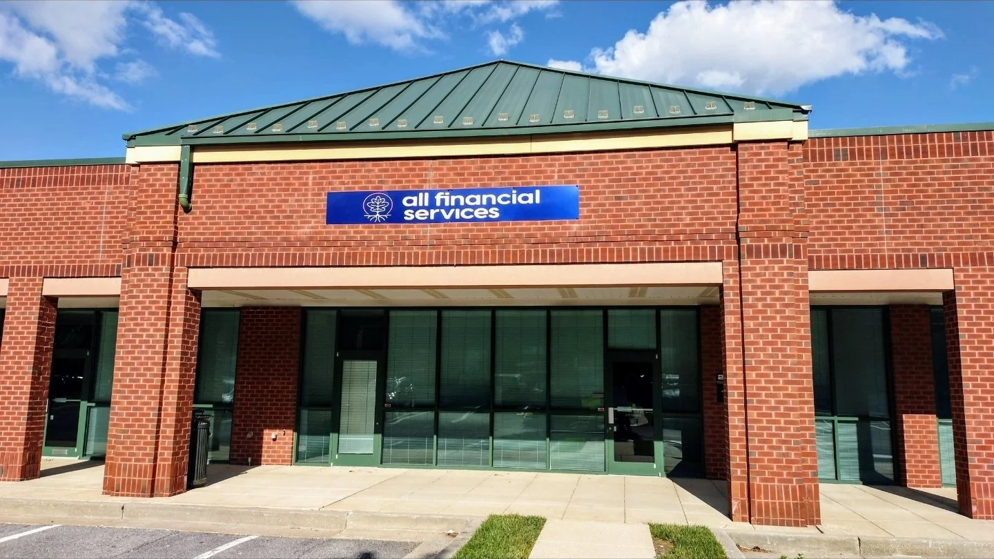 Brick building with a green metal roof and large glass windows, labeled 'all financial services' on a blue sign.