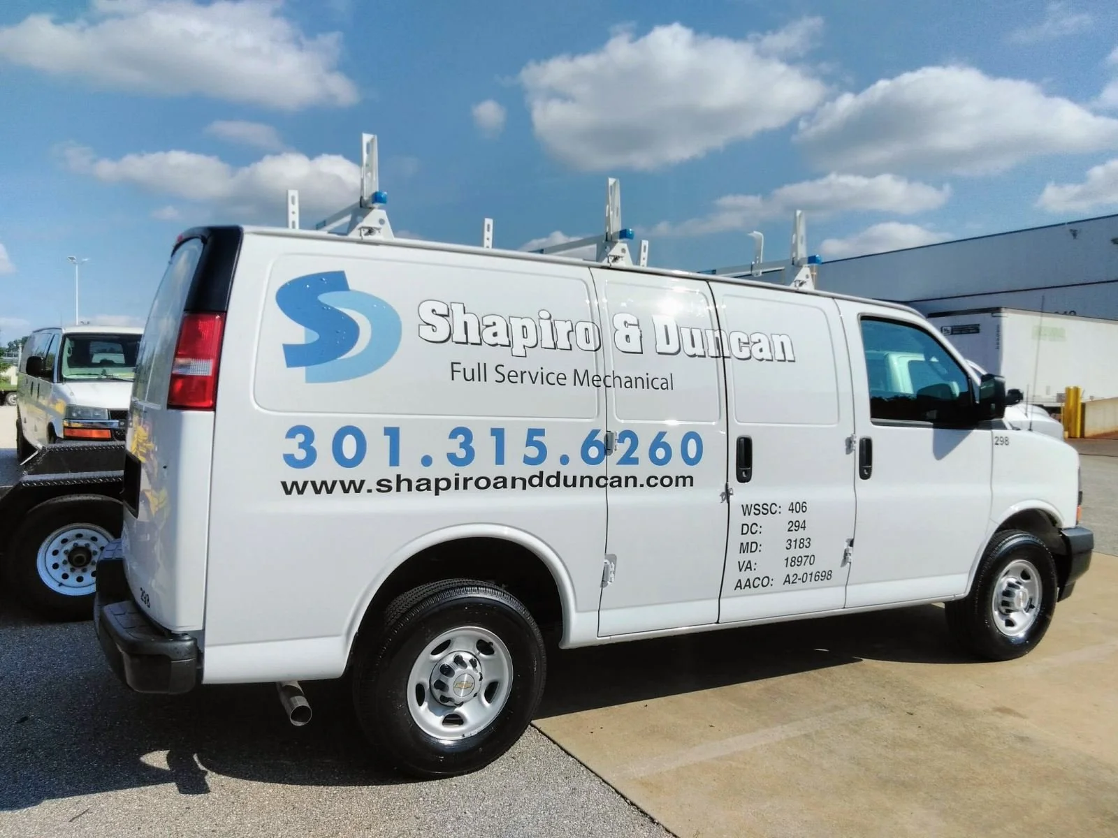 A white service van with the logo and contact information for Shapiro & Duncan on the side, parked outdoors on a concrete lot under a partly cloudy sky.