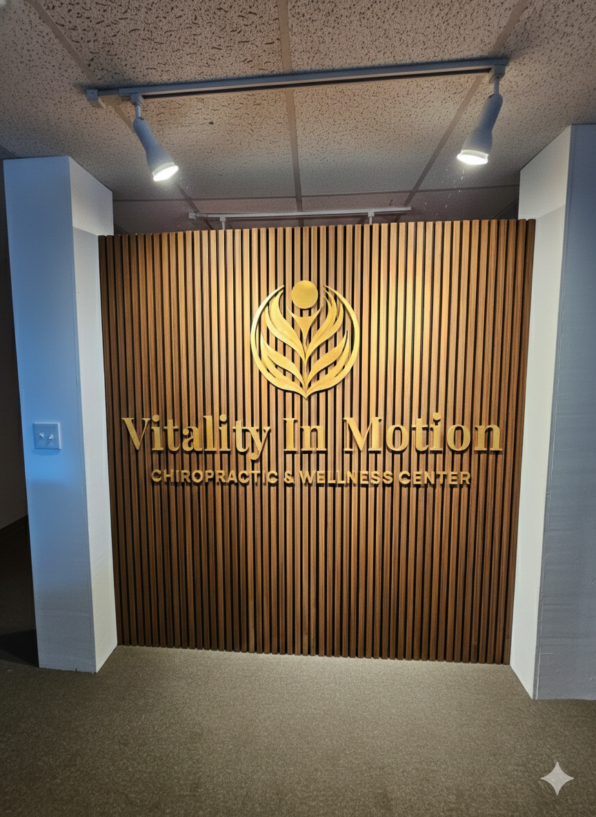 Wooden wall with a logo and gold lettering that reads 'Vitality in Motion Chiropractic & Wellness Center.'