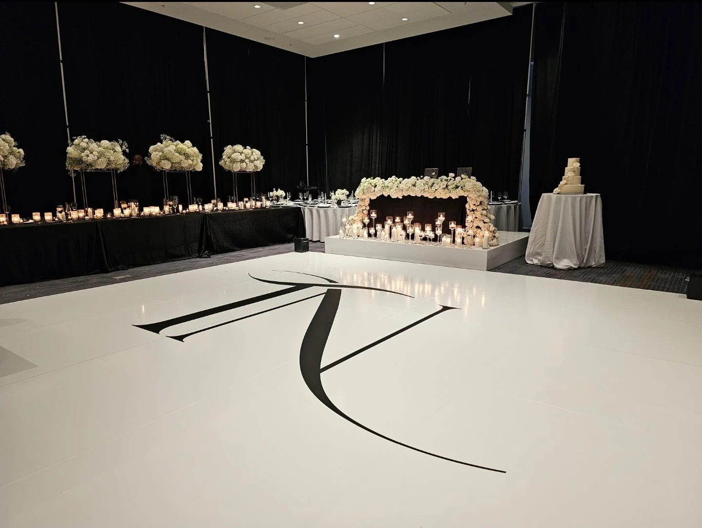 Wedding reception setup with floral arrangements, candles, and a wedding cake. The dance floor features a large black letter 'Z' on a white background.